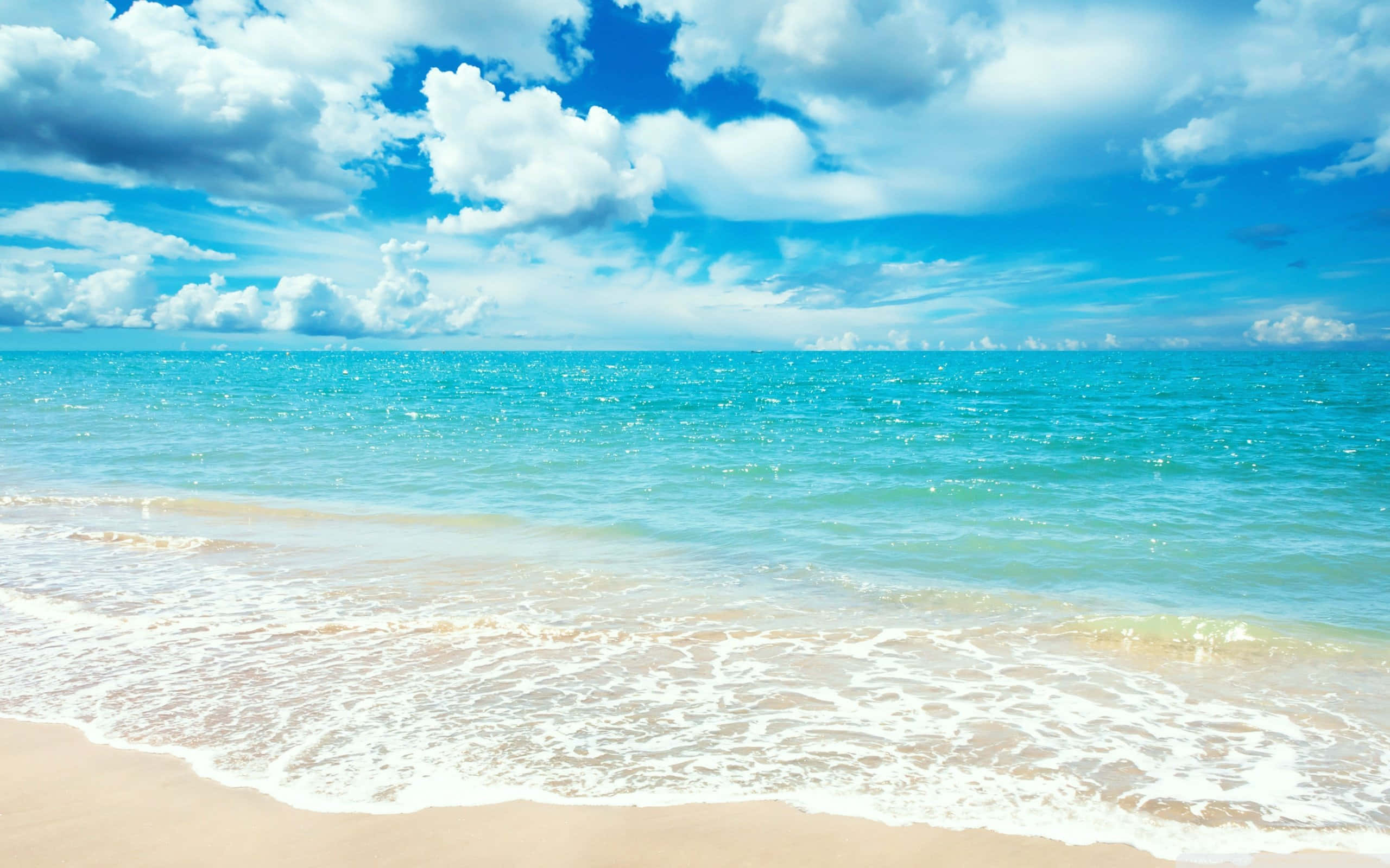 High Resolution Beach 桌布 壁紙 — 陽光普照的碧綠海浪輕輕拍打著金色沙灘，在點綴著蓬鬆白雲的湛藍天空下。