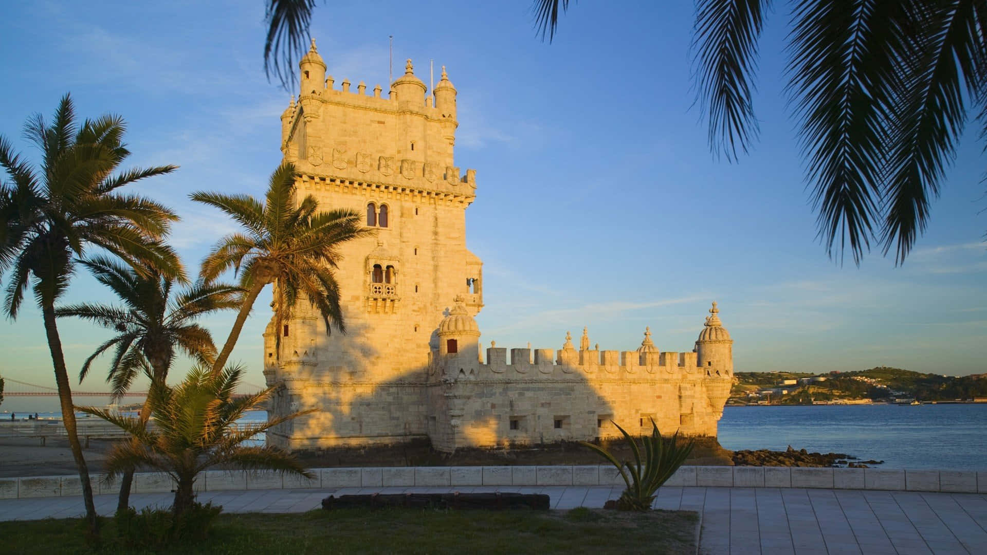 Portugal 桌布 壁紙 — 陽光普照的貝倫塔在金色時刻聳立在塔霍河畔，被棕櫚樹環繞。