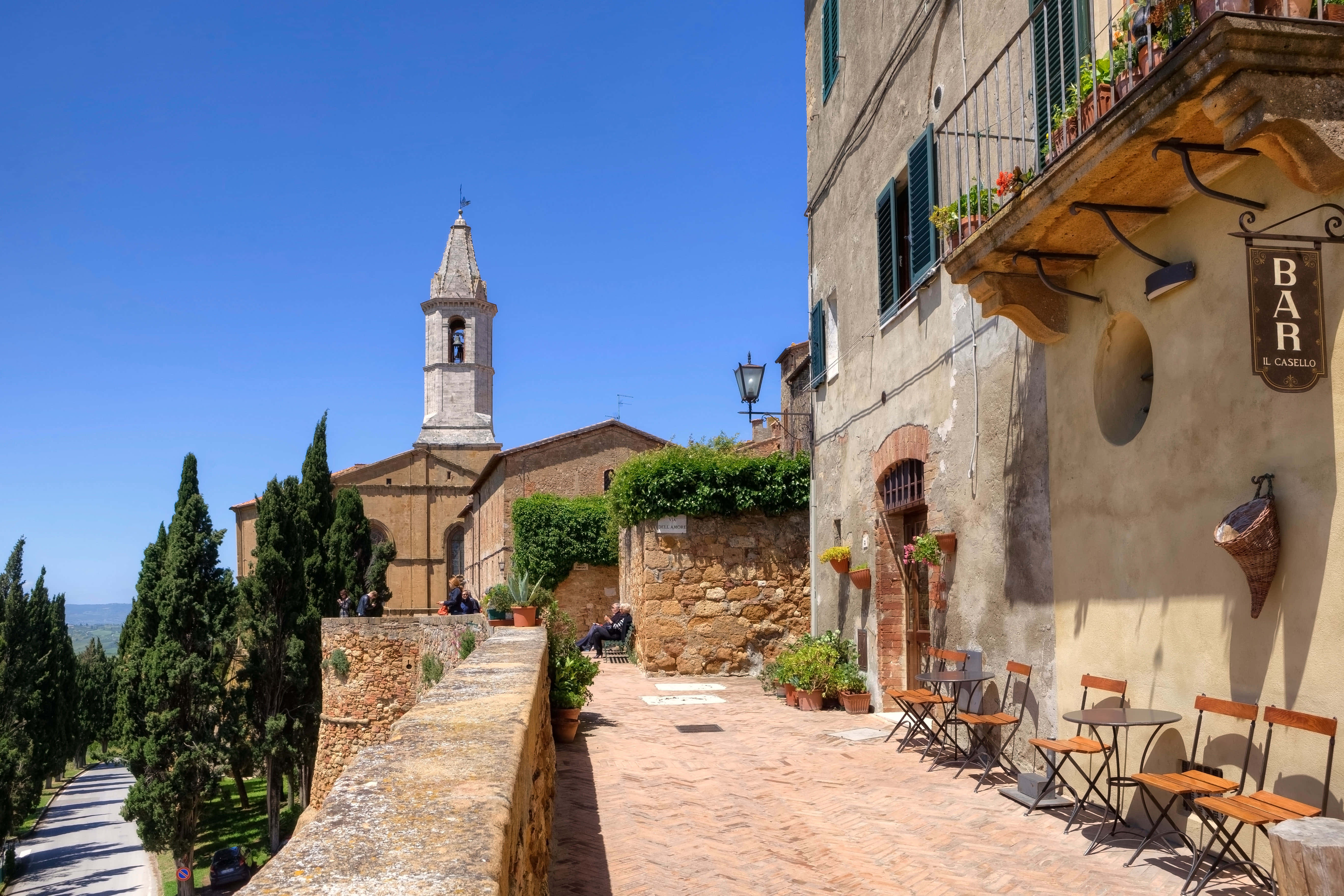 Tuscany 桌布 壁紙 — 陽光普照的鵝卵石小巷，位於古樸的義大利村莊，有石頭建築、陶土屋頂和教堂鐘樓，襯著清澈的藍天。