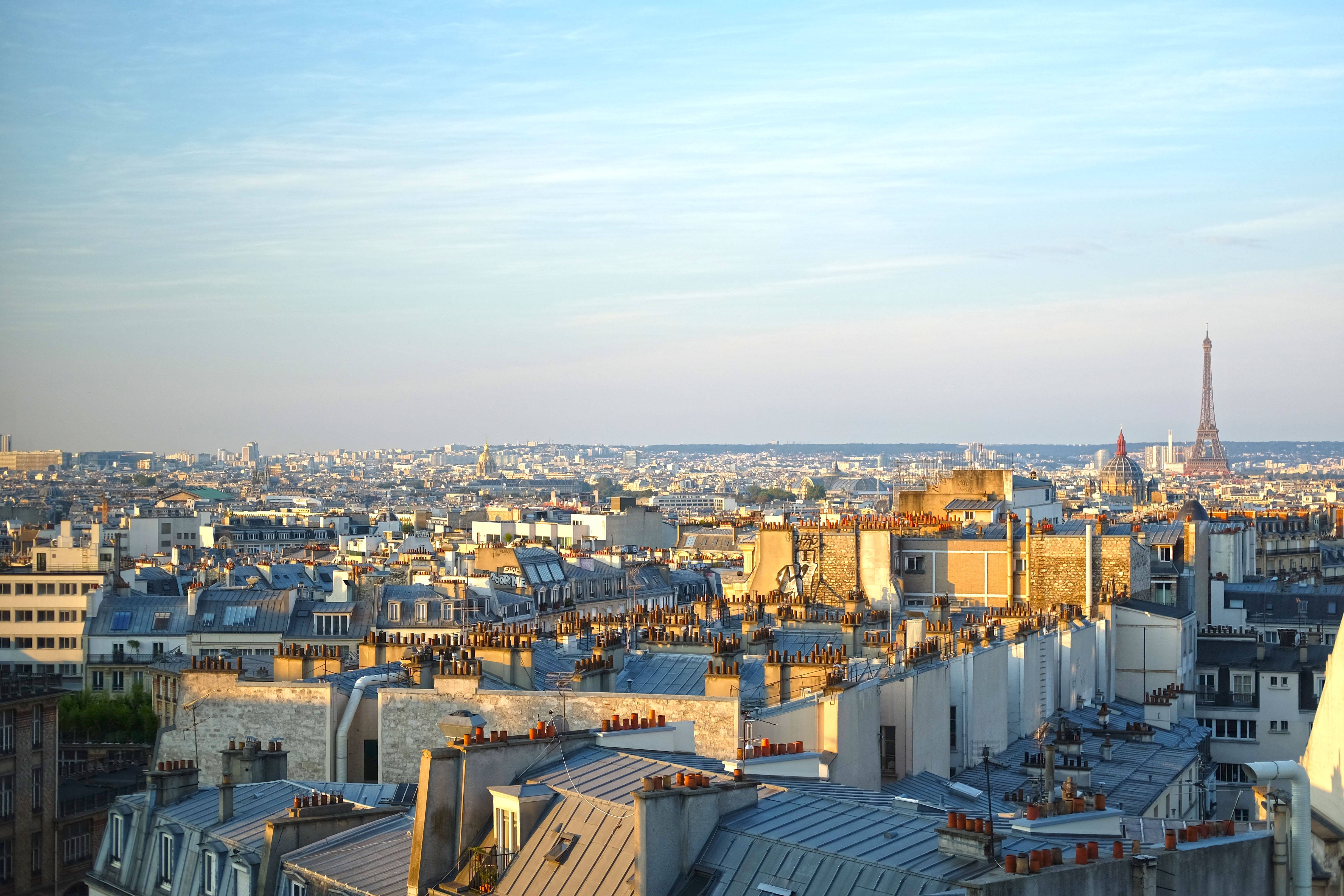 Eiffel Tower 桌布 壁紙 — 陽光沐浴著巴黎的屋頂，散發金色溫暖，遠處的艾菲爾鐵塔在柔和的藍天下聳立。