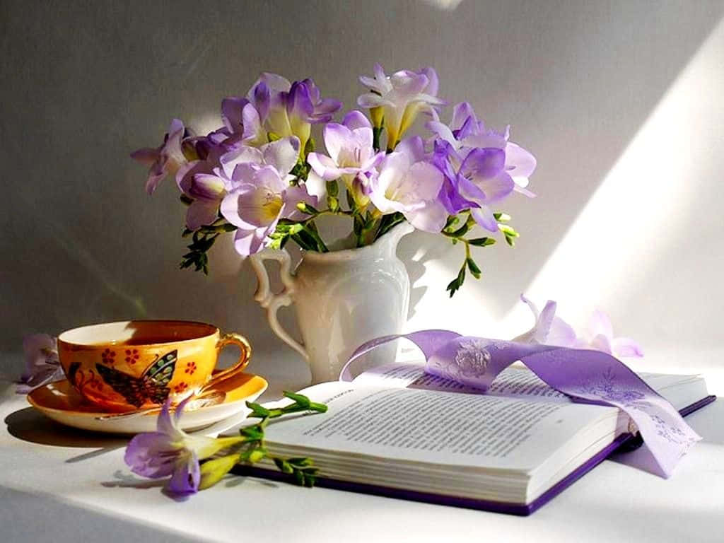 書本 桌布 壁紙 — 陽光灑落在一個白色花瓶中的紫色小蒼蘭、一本打開的書和一個冒著蒸氣的黃色茶杯的靜物畫上。