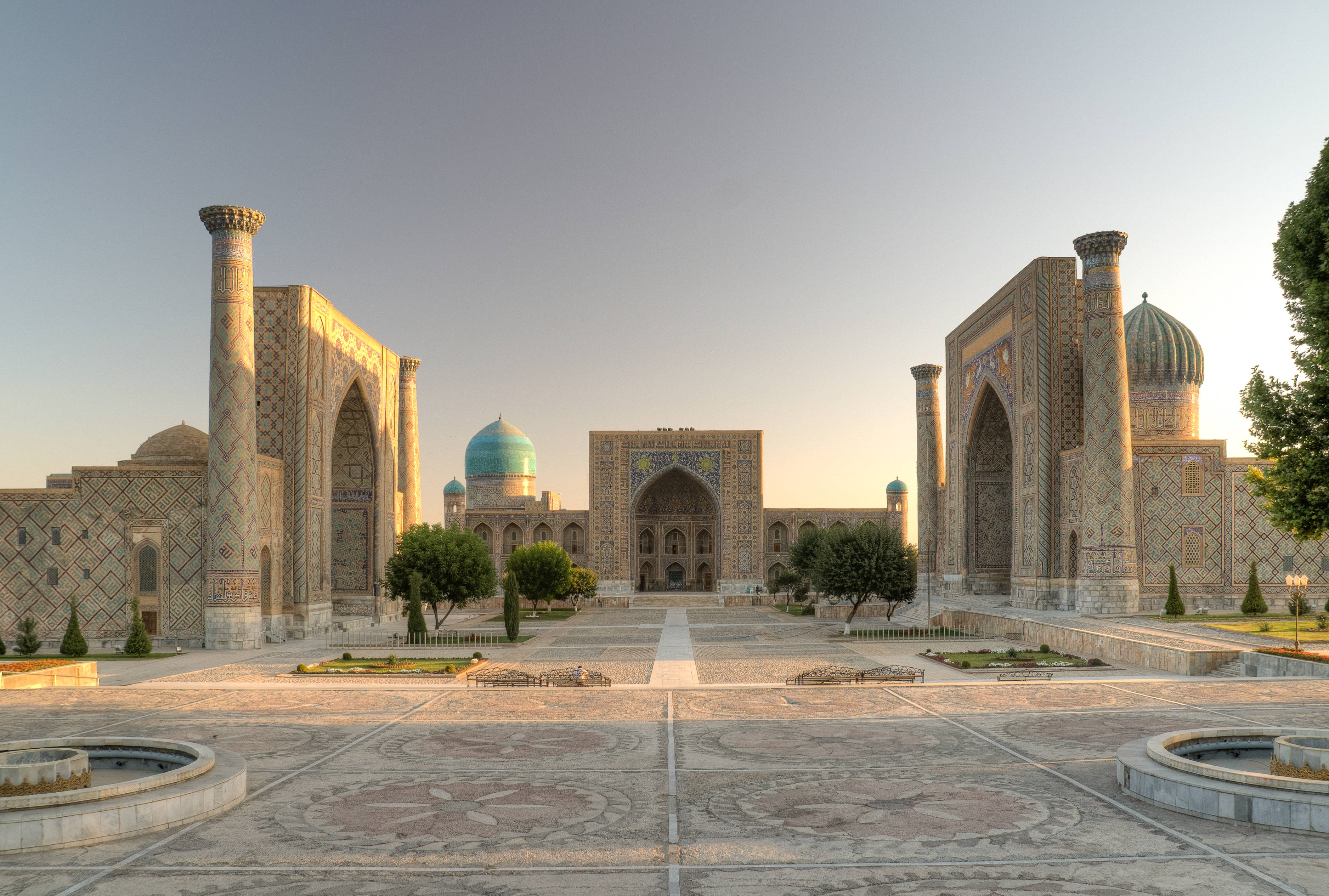 Uzbekistan 桌布 壁紙 — 陽光灑落在古老的伊斯蘭建築上，映照著廣闊庭院中的綠松石圓頂和精緻的瓷磚工藝。