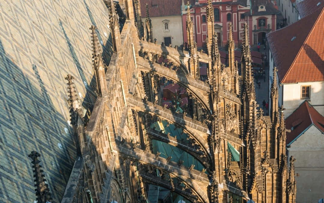 Gothic Architecture 桌布 壁紙 — 陽光灑落在哥德式大教堂屋頂複雜的石雕窗飾和尖塔上，背景是紅瓦屋頂。