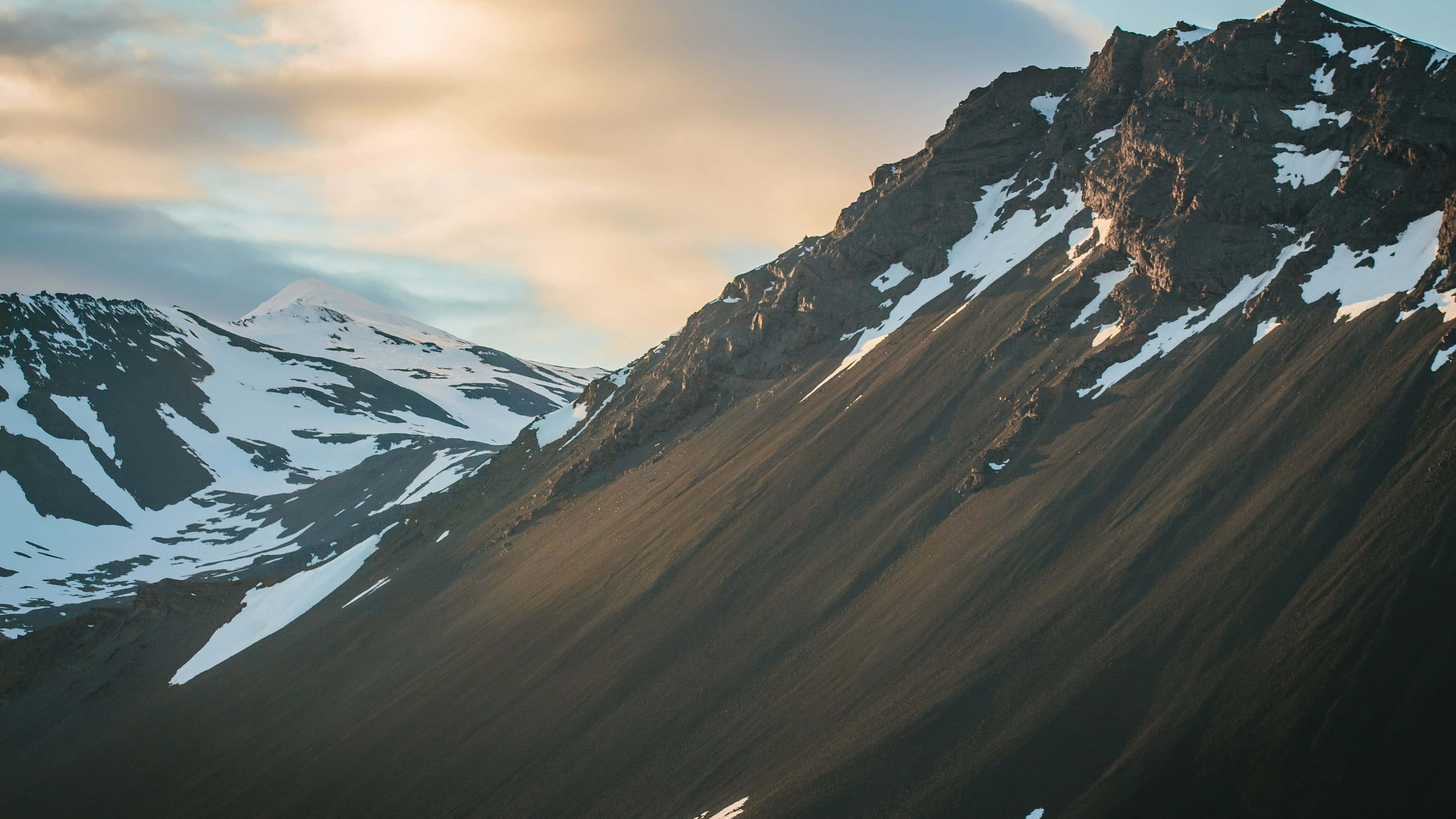 Iceland Desktop 桌布 壁紙 — 陽光灑落在積雪的山峰上，在柔和的雲天下呈現金色溫暖。