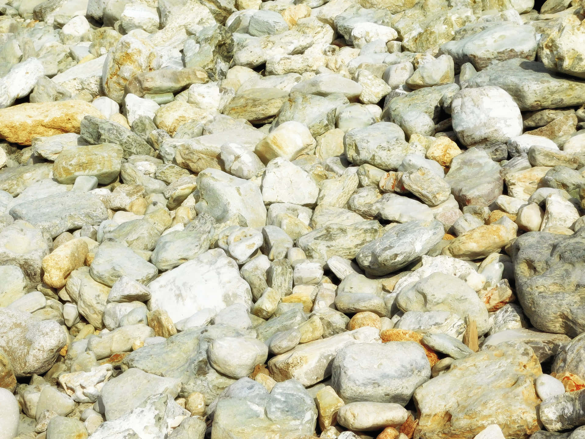 Stone texture 壁紙 — 陽光照射下的特寫，各種灰色、米色和白色的河石以自然粗糙的質感堆疊在一起。