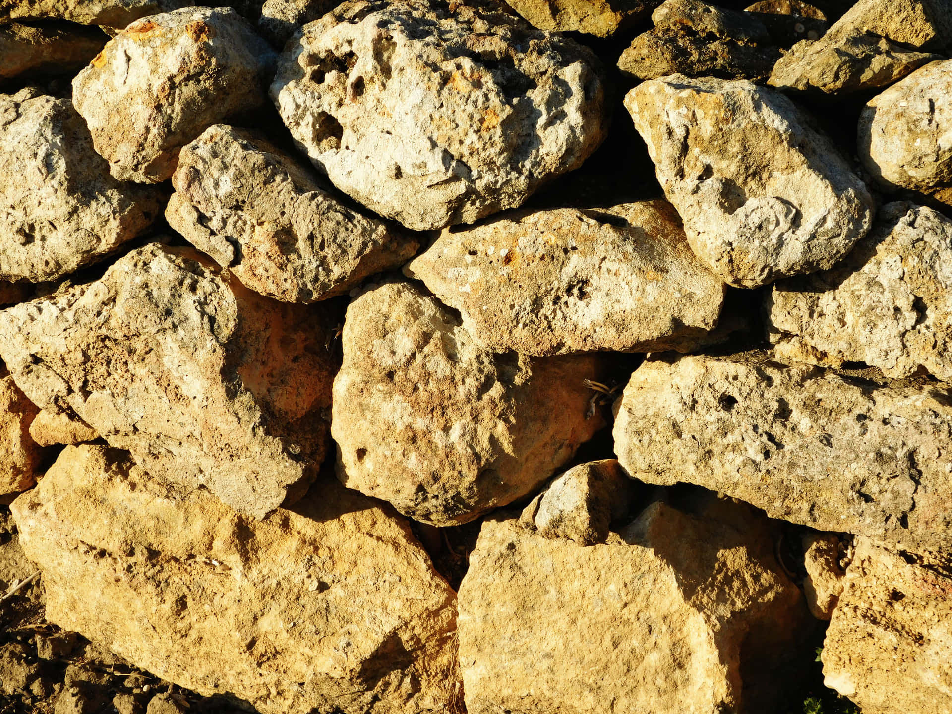 Stone texture 壁紙 — 陽光照射下的特寫，粗糙質感的堆疊田野石塊，以溫暖的大地色調形成質樸的牆壁。