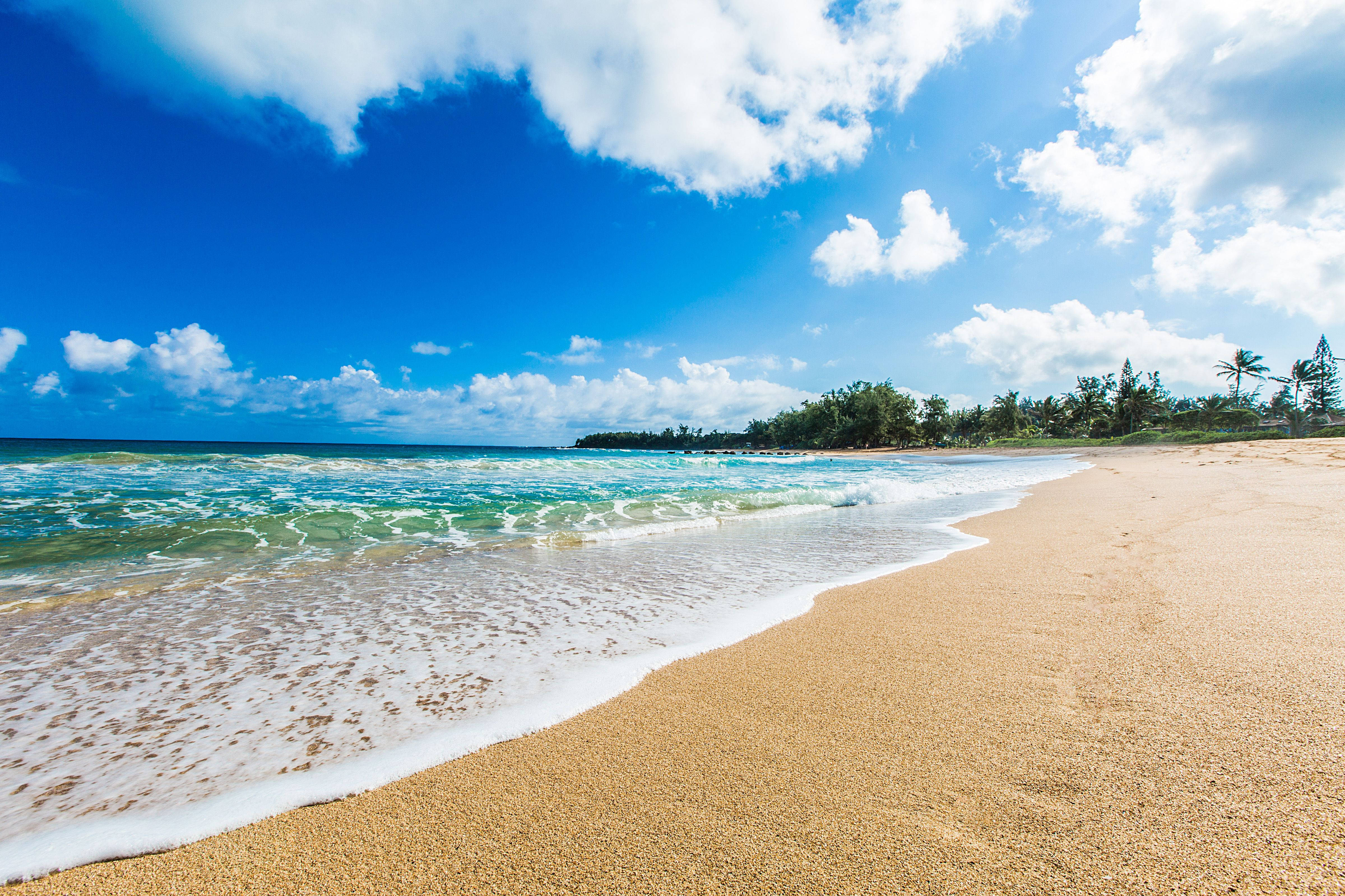 Beach Scenes Desktop 桌布 壁紙 — 陽光照射下的碧綠海浪拍打著金色沙灘，上方是點綴著蓬鬆白雲的湛藍天空。