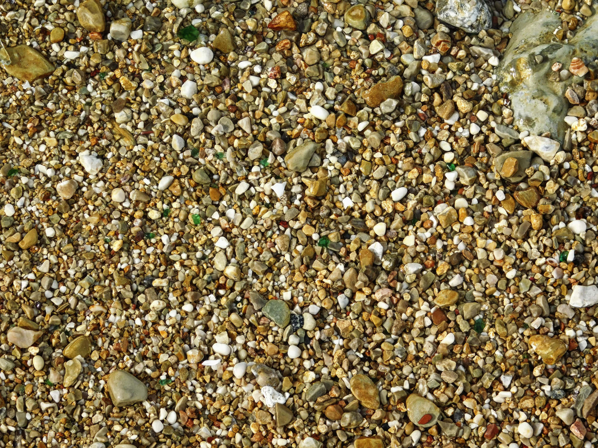 Stone texture 壁紙 — 陽光照射下的鵝卵石和礫石近距離特寫，呈現大地色調，散落著綠色玻璃碎片。