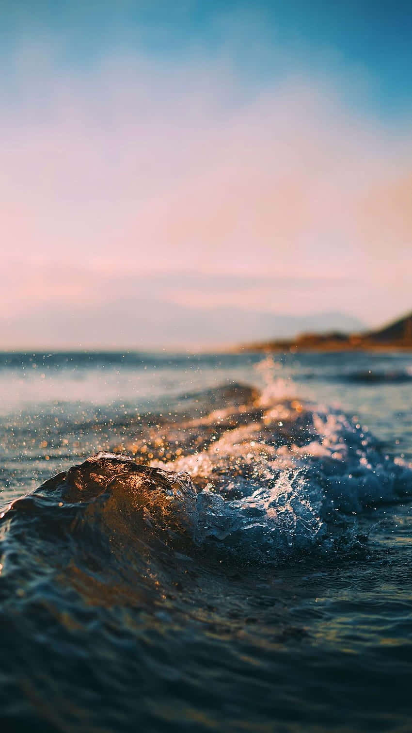 Ocean Aesthetic Phone 桌布 壁紙 — 陽光照射的海浪特寫，浪花飛濺，閃爍的水珠映襯著柔和粉紅與藍色的天空。