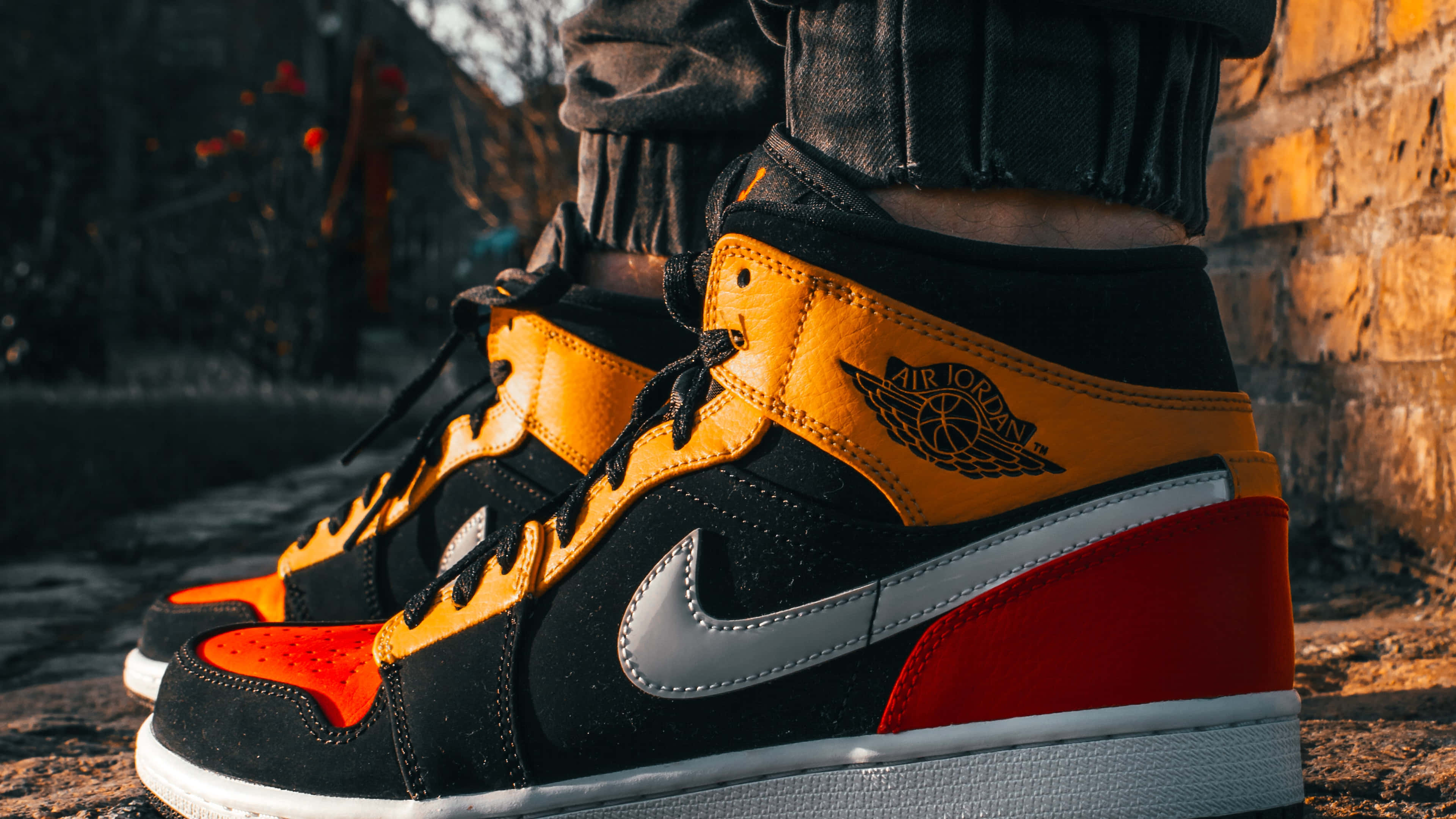桌布 壁紙 — 陽光照射的磚牆背景下，鮮豔的黑色、橙色和紅色 Air Jordan 運動鞋特寫。