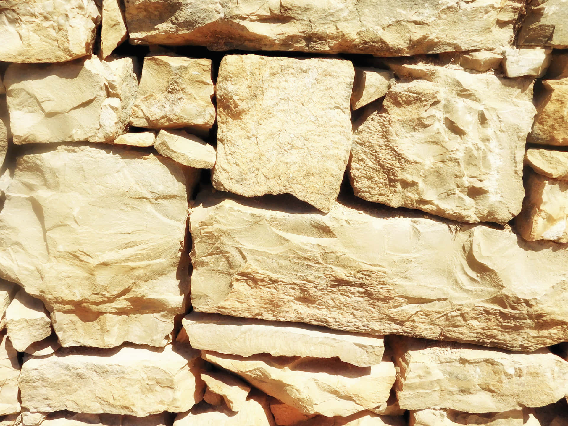 Stone texture 壁紙 — 陽光照射的米色石牆，粗糙紋理的磚塊以不均勻的行堆疊。