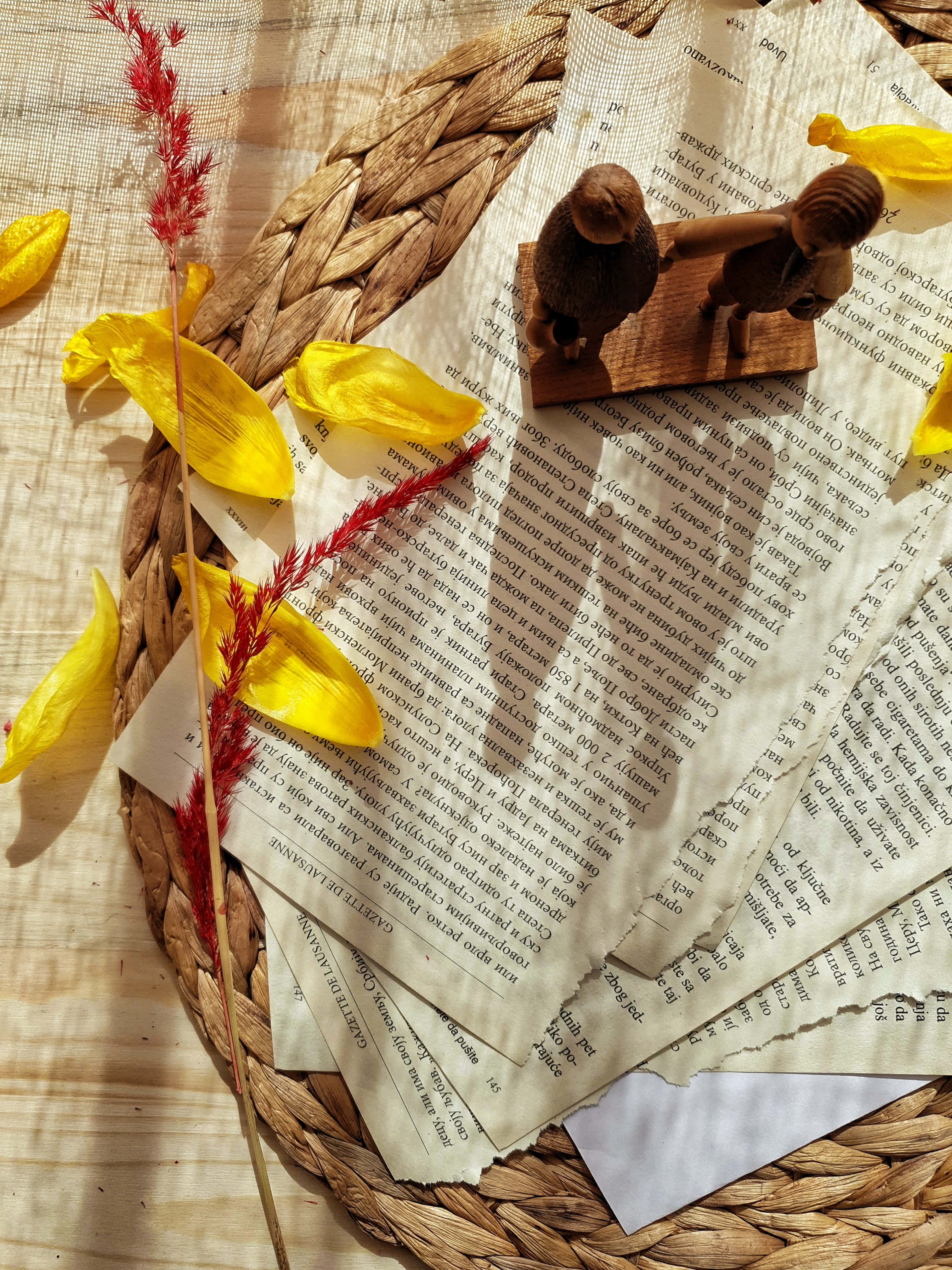 basket 桌布 壁紙 — 陽光照射的編織籃子裡裝著復古書頁、黃色花瓣和木製小雕像，營造出舒適的文學靜物。