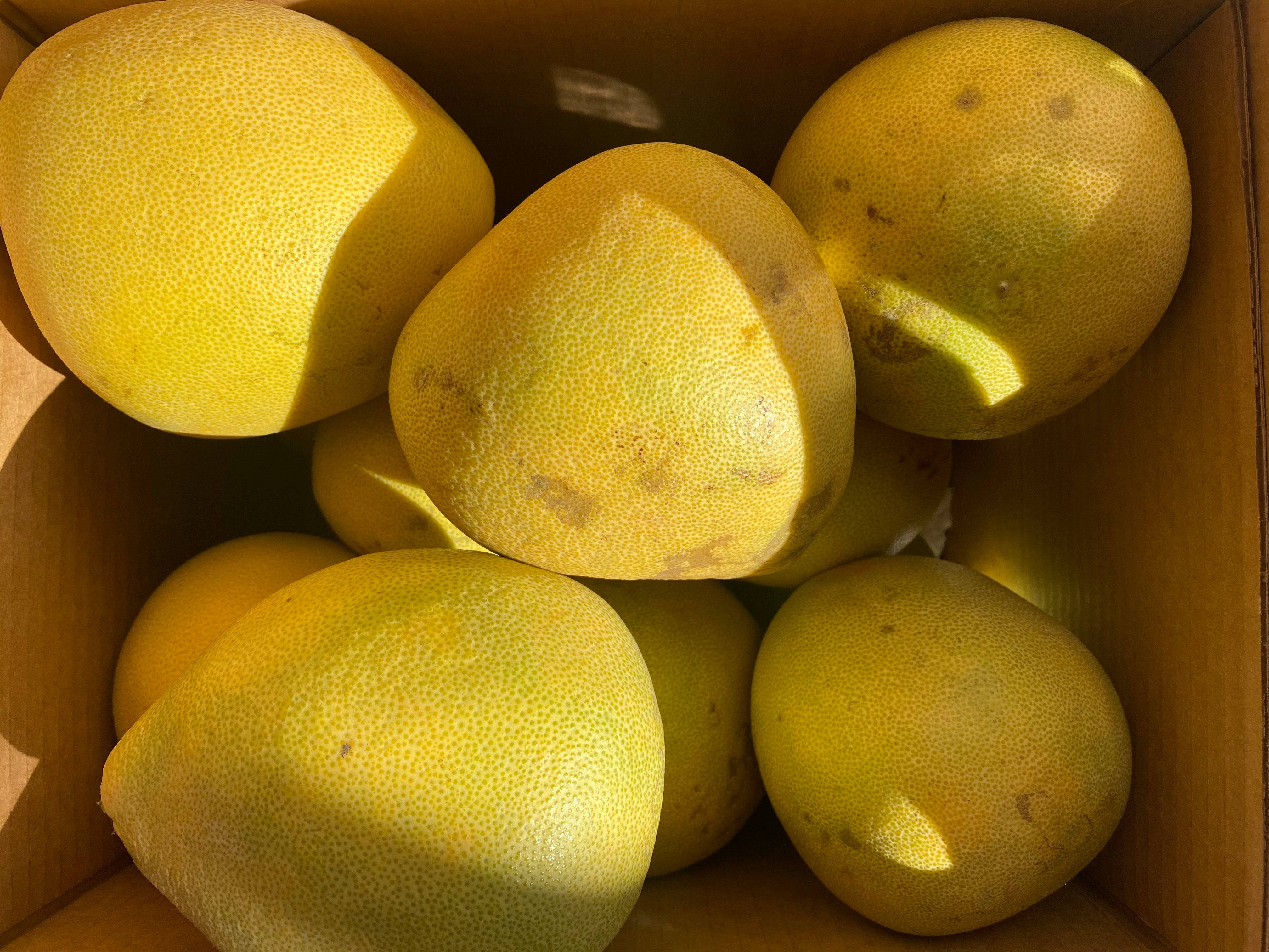 Fruits 桌布 壁紙 — 陽光照射的黃色柚子，帶有紋理的外皮，裝滿一個紙箱，特寫俯拍。