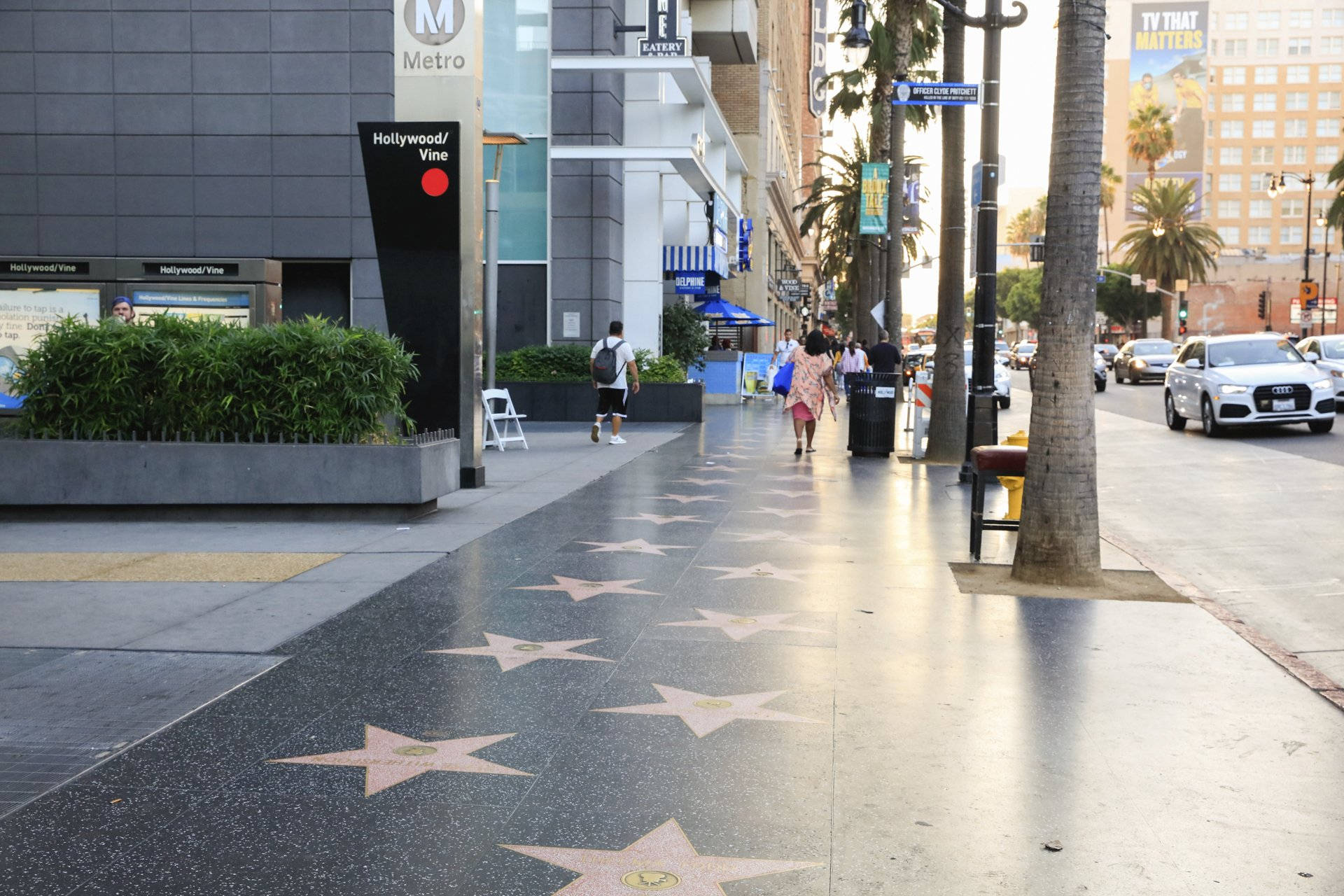 walk 桌布 壁紙 — 陽光照耀下的好萊塢星光大道星星嵌在人行道上，行人與棕櫚樹排列在繁華的都市街道兩旁。