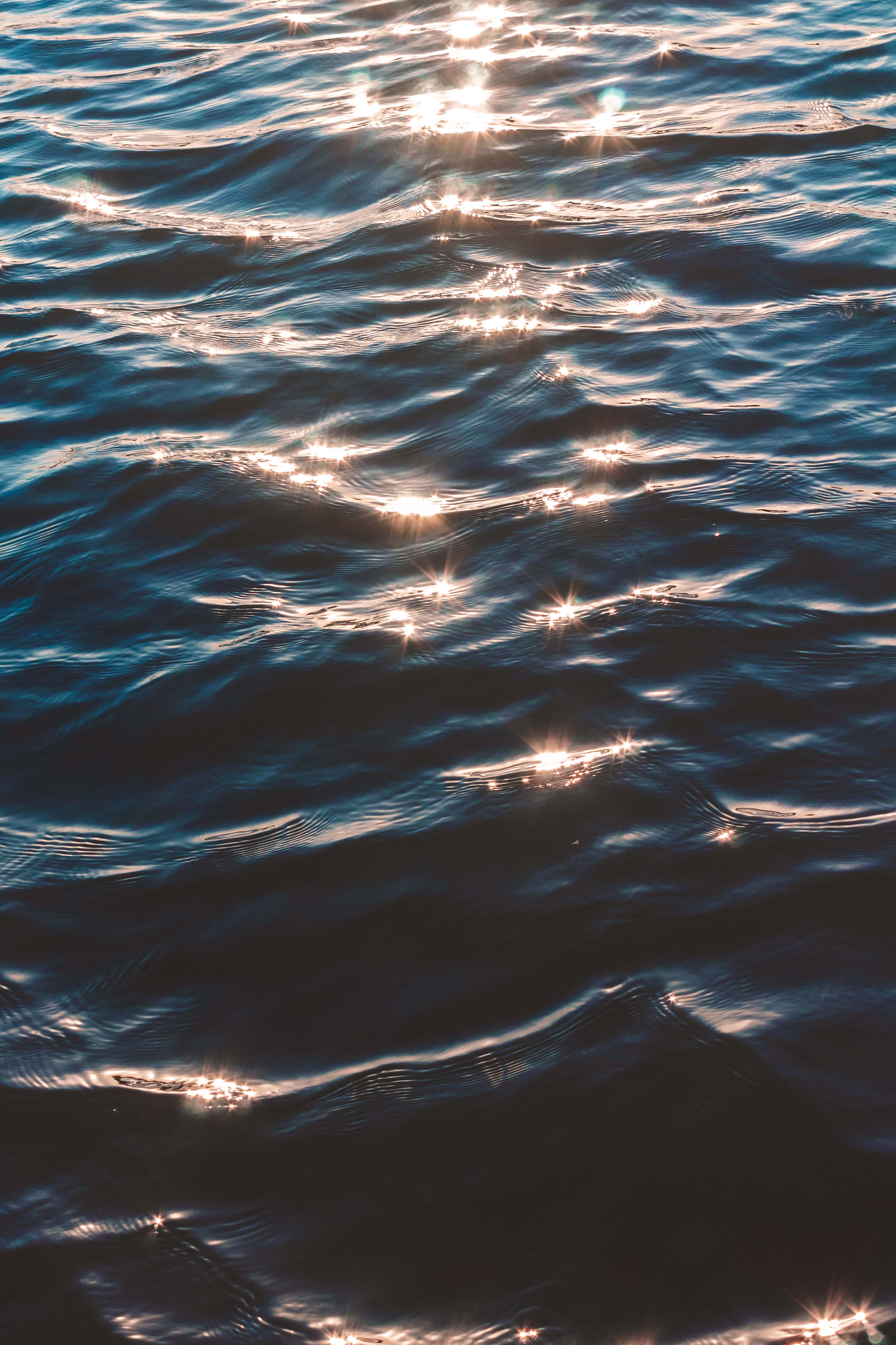 Ocean Aesthetic Phone 桌布 壁紙 — 陽光照耀在深藍色海浪上，在紋理水面上形成閃爍的倒影。