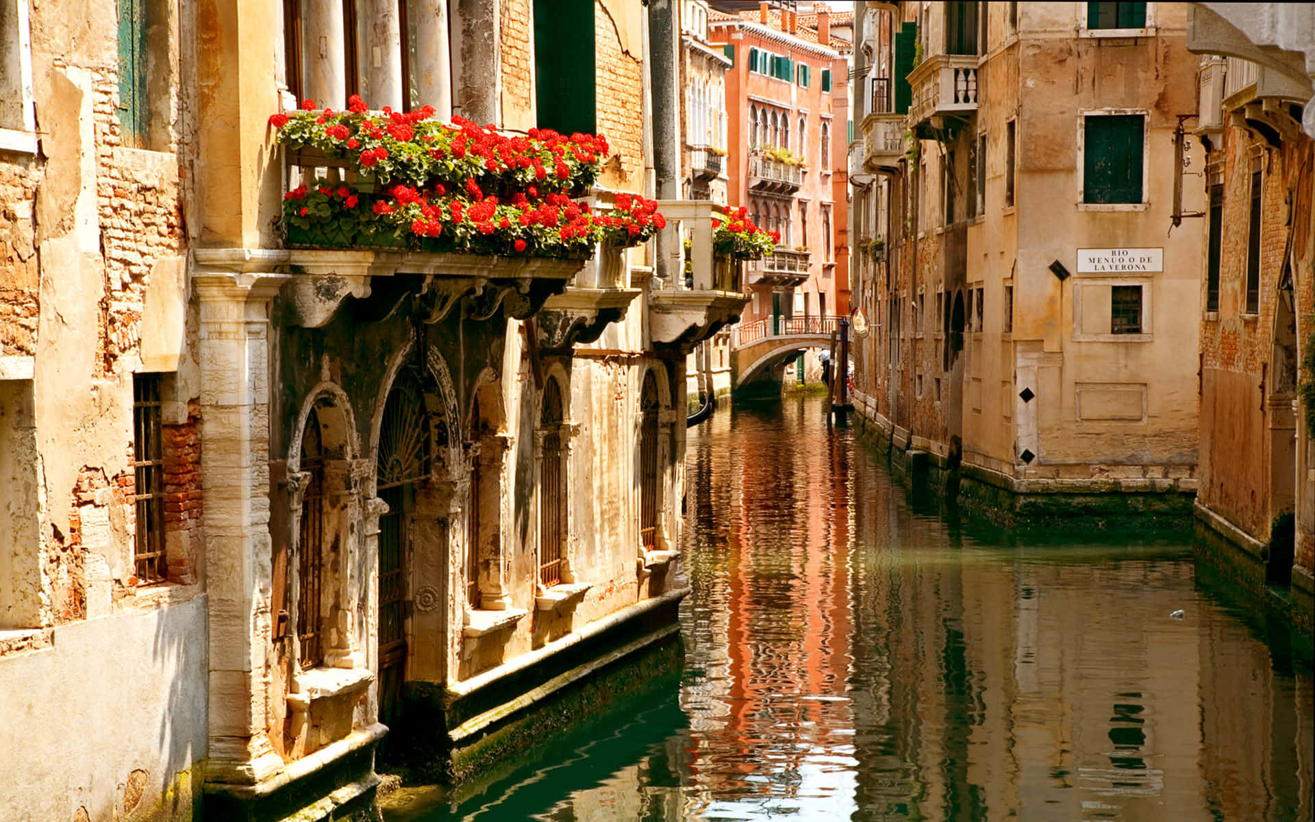 Italian 桌布 壁紙 — 陽光照耀的威尼斯運河，兩旁是歷史建築，鮮紅色的花盒在平靜的水面上倒映。