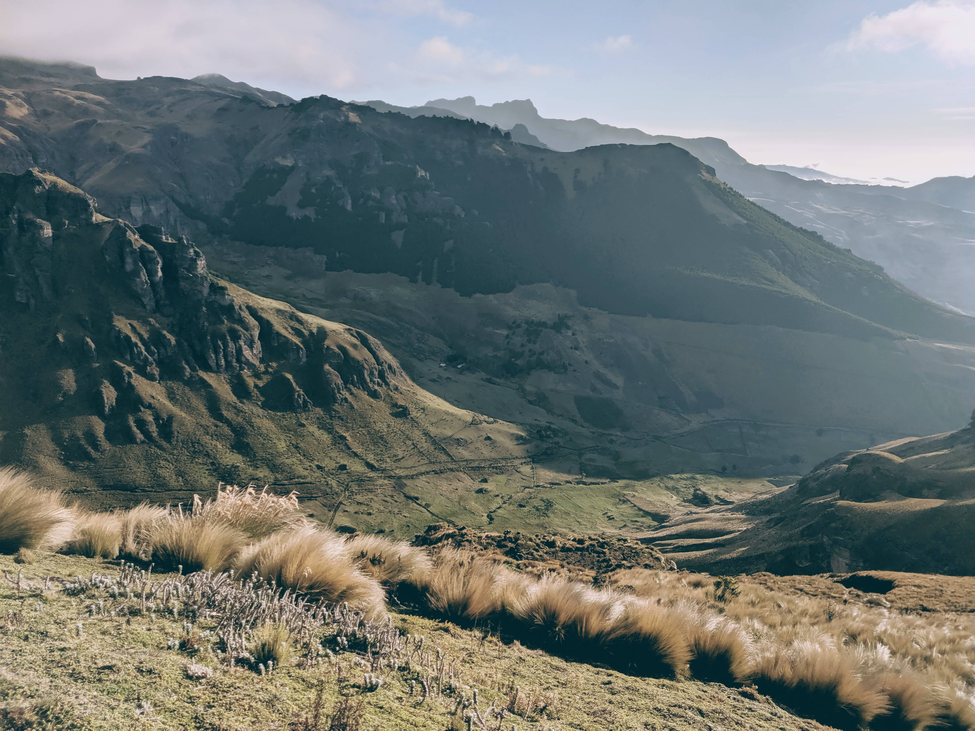 Ecuador 桌布 壁紙 — 陽光照耀的山谷，前景是金色的草地，崎嶇的山峰在霧濛濛的遠方逐漸消失。