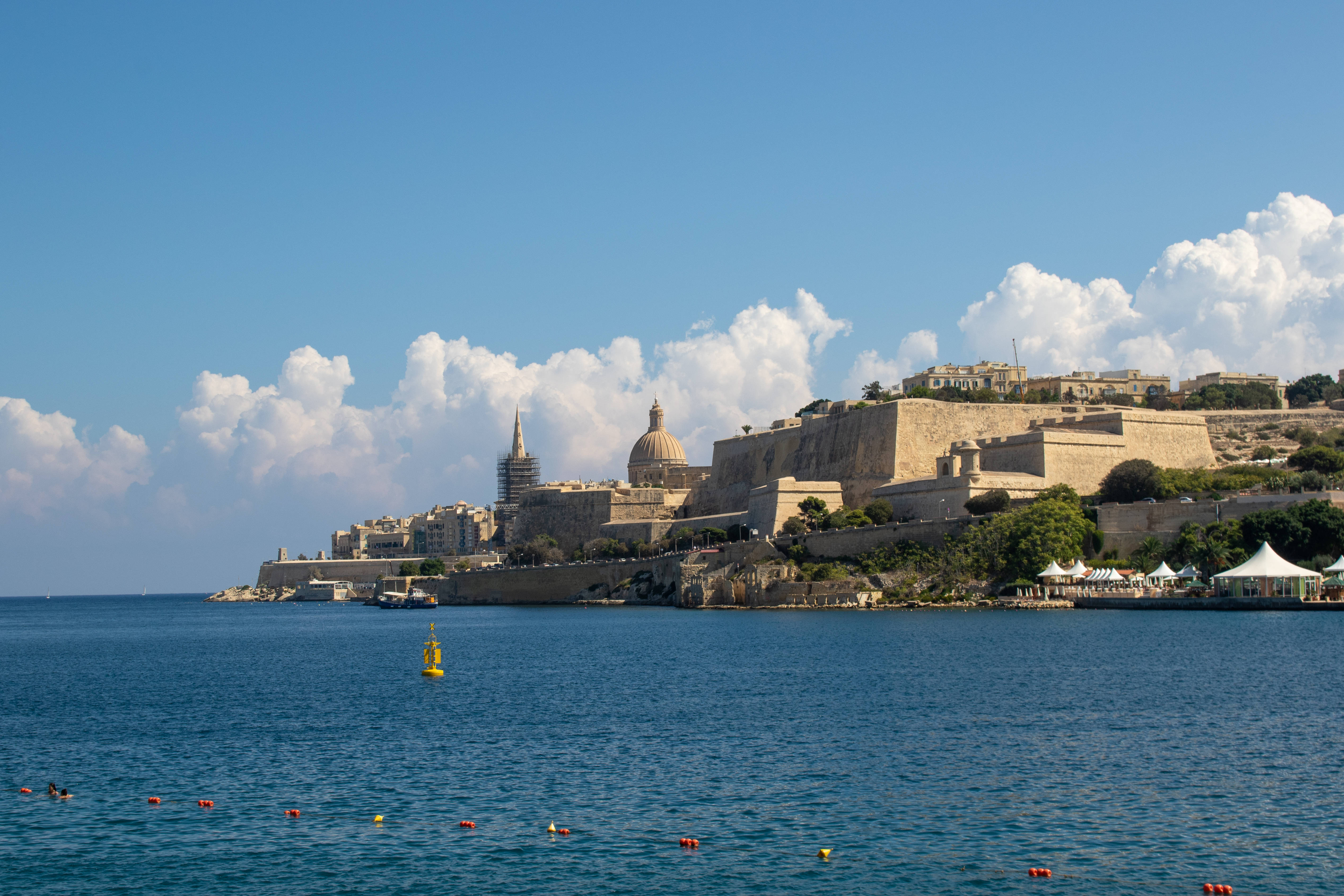 Malta 桌布 壁紙 — 陽光照耀的歷史堡壘矗立於海岸懸崖上，俯瞰深藍色大海與上方白雲。