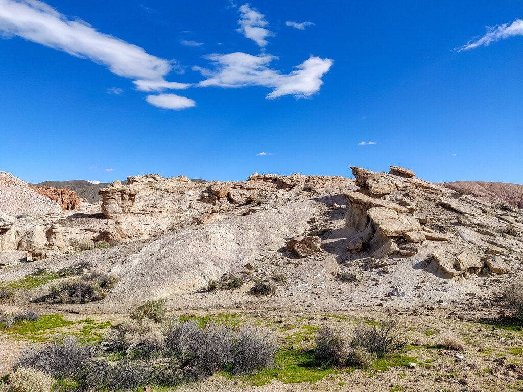 Red Rock 桌布 壁紙 — 陽光照耀的沙漠景觀，層狀岩石結構和稀疏的綠色灌木，在明亮的藍天下有縷縷白雲。