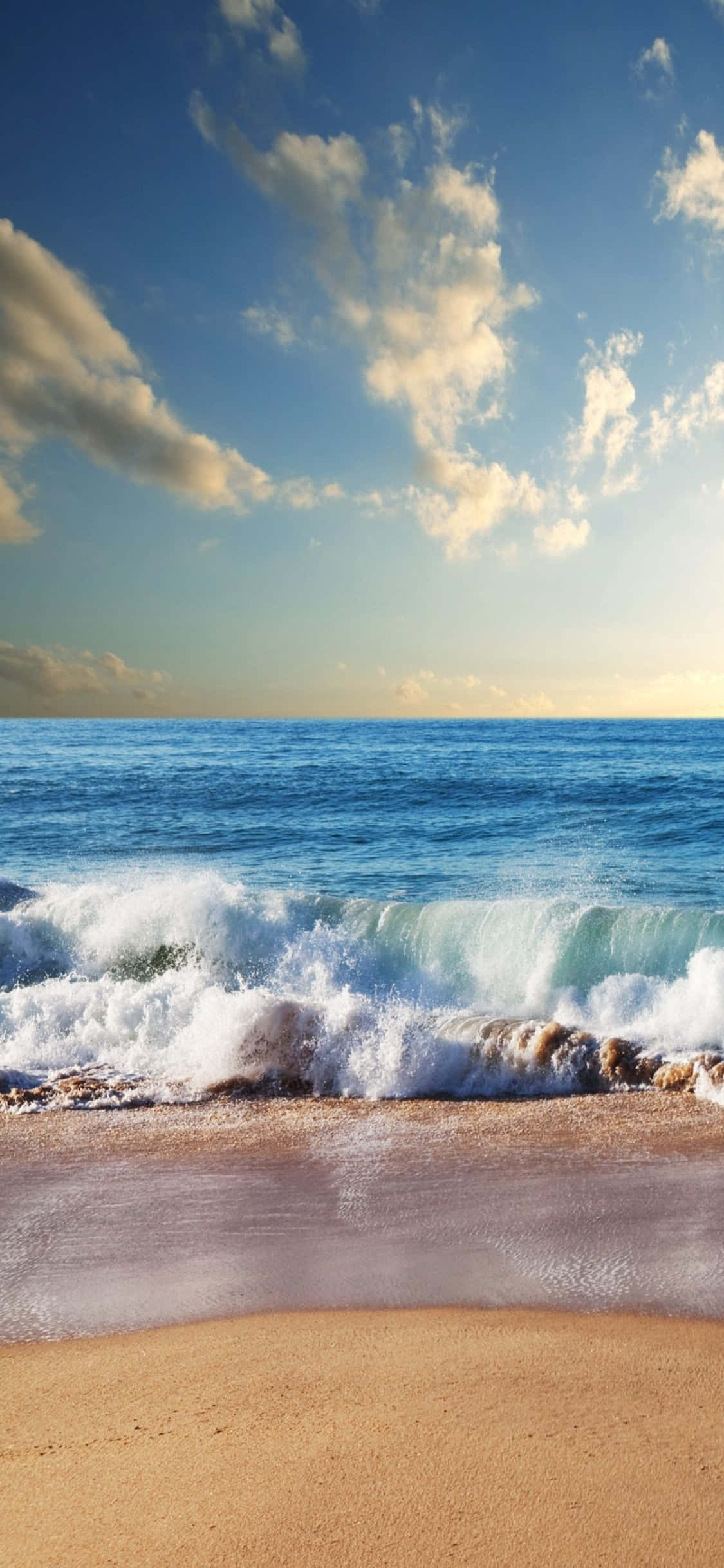 海灘 桌布 壁紙 — 陽光照耀的海浪拍打在金色沙灘上，天空湛藍，白雲點綴。