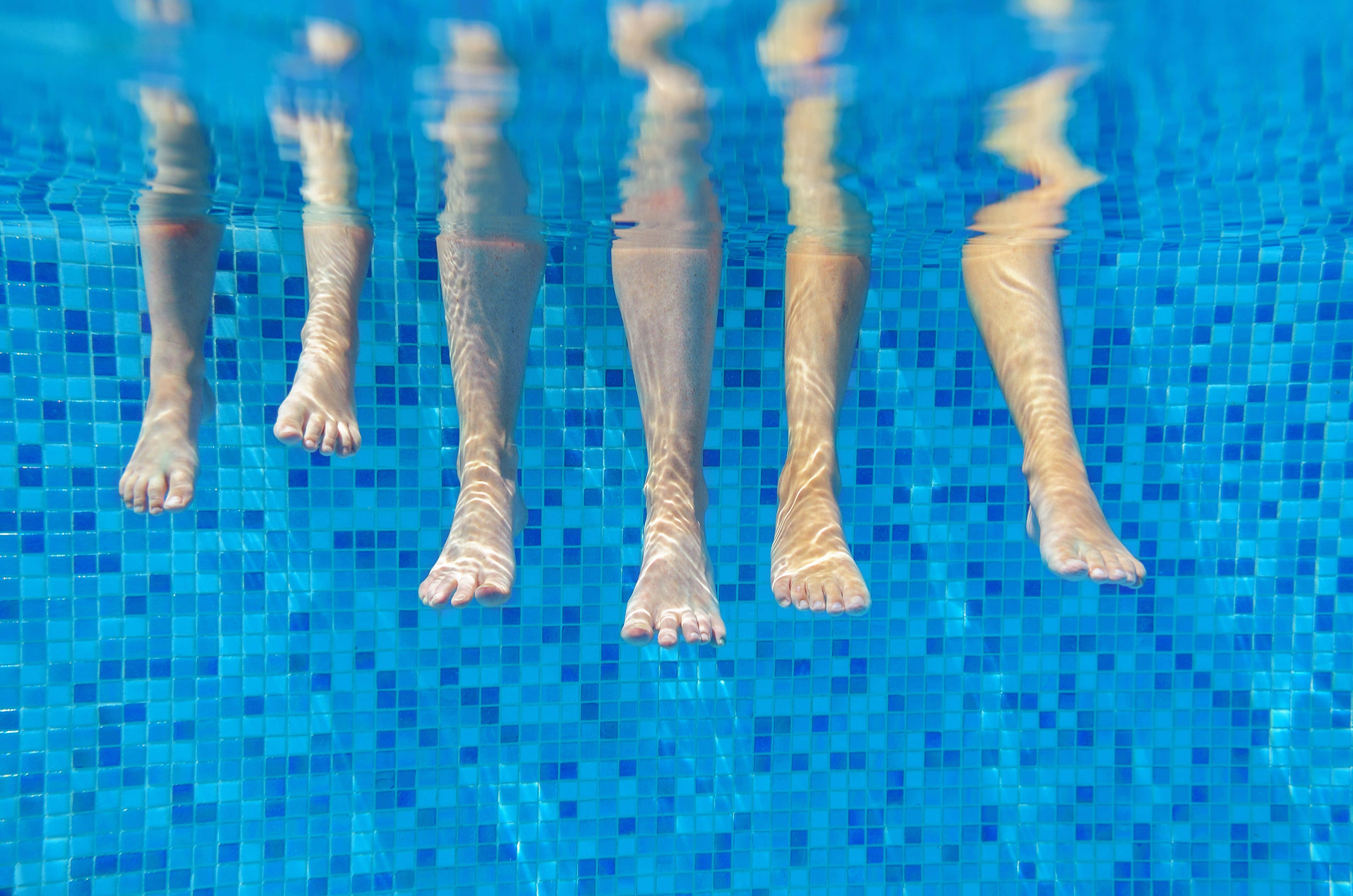 pool 桌布 壁紙 — 陽光照耀的游泳池中，五隻赤腳放在藍色馬賽克瓷磚上的水下視圖。