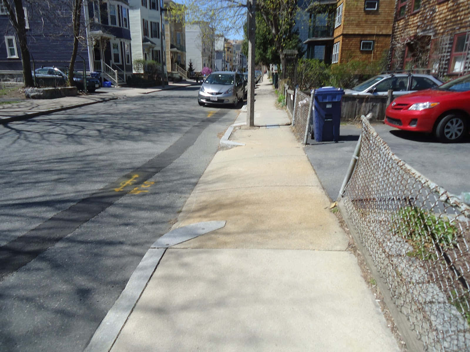 Sidewalk 桌布 壁紙 — 陽光照耀的都市人行道，兩旁停滿汽車和色彩繽紛的連棟房屋，投下樹影。