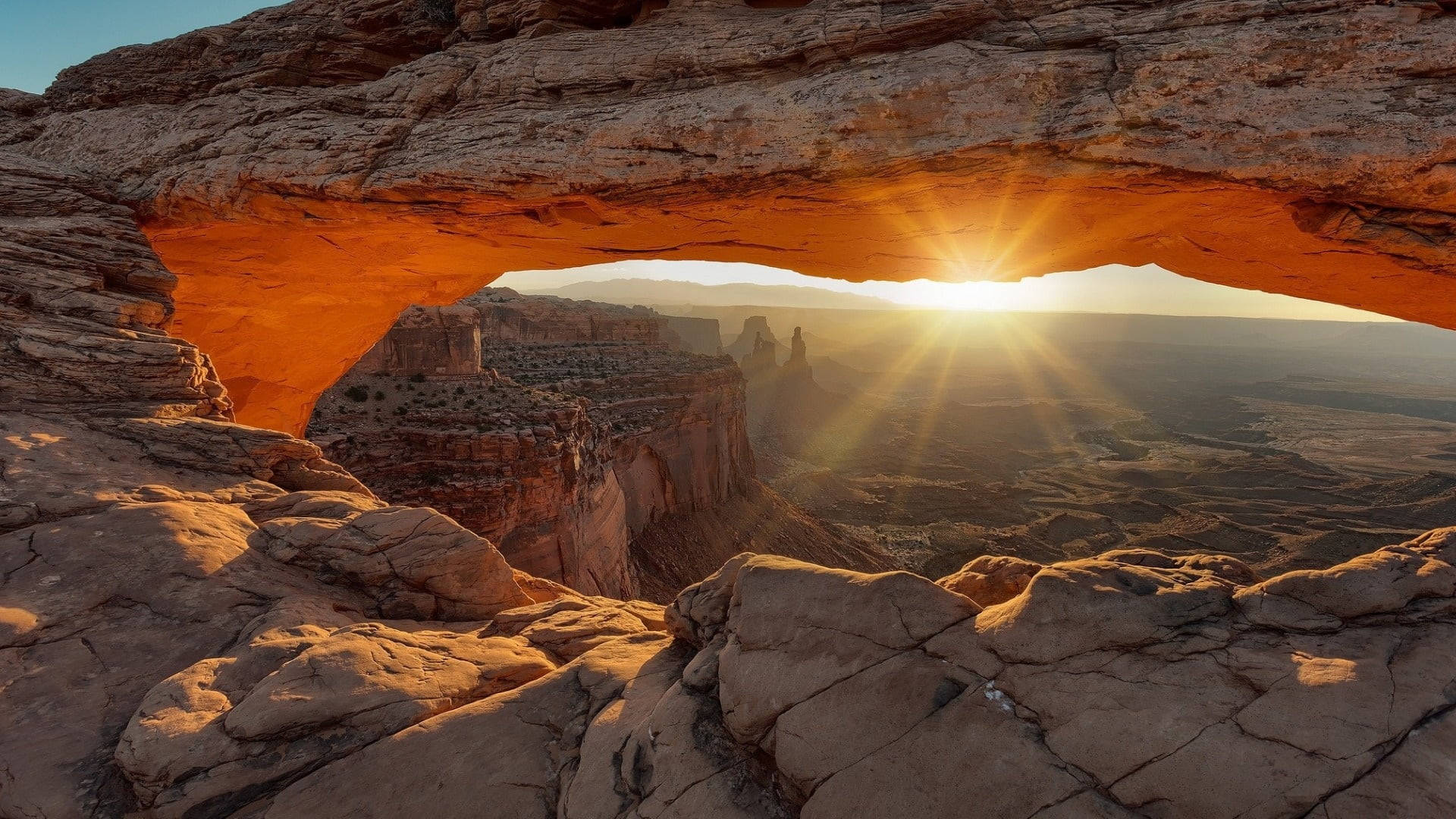 Canyonlands National Park 桌布 壁紙 — 陽光穿透一個巨大的橙色砂岩拱門，框住廣闊的沙漠峽谷，正值黃金時刻。