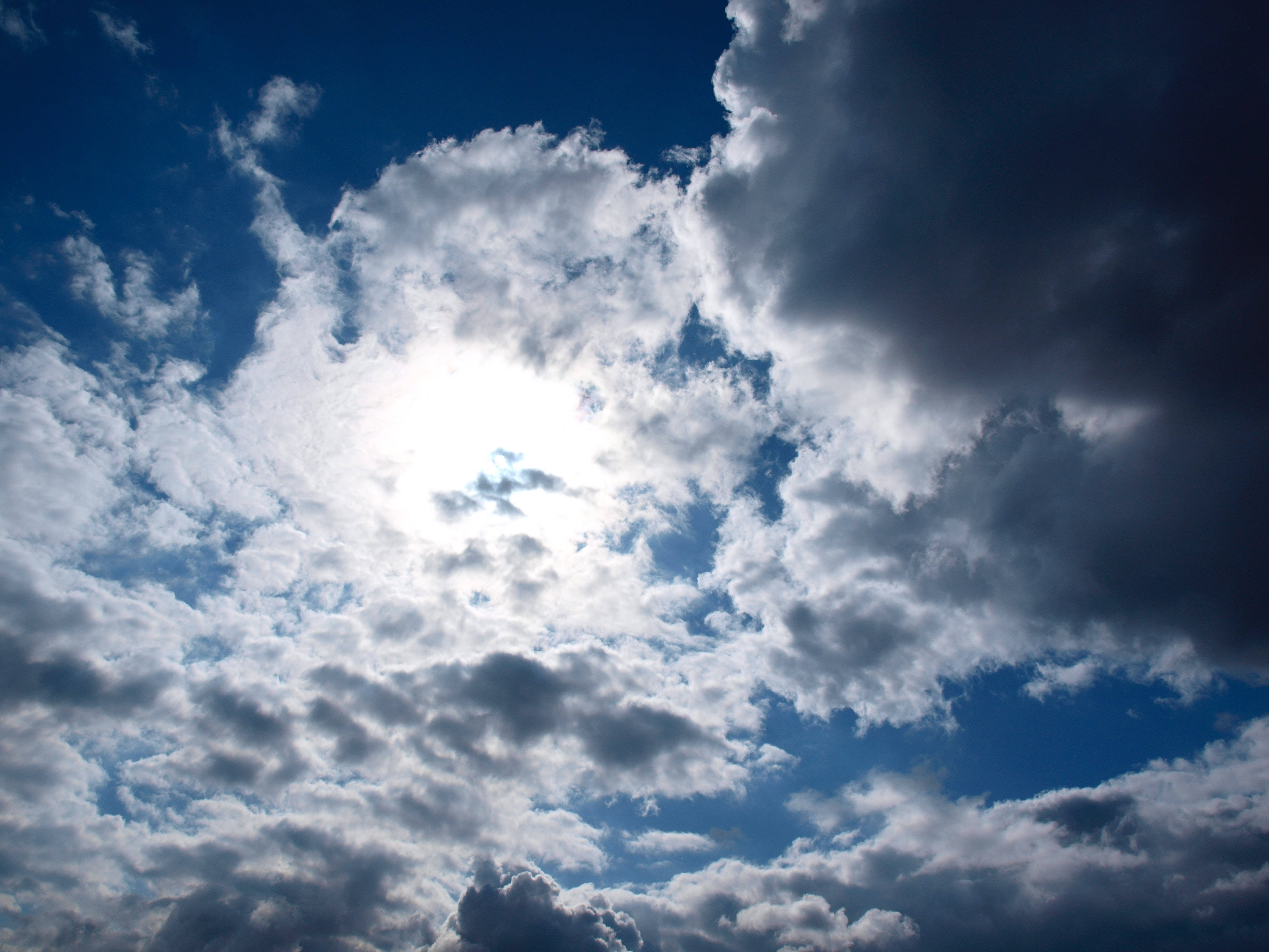 Cloudy Sky 桌布 壁紙 — 陽光穿透充滿蓬鬆白色和深灰色雲層的戲劇性天空，背景是深藍色。
