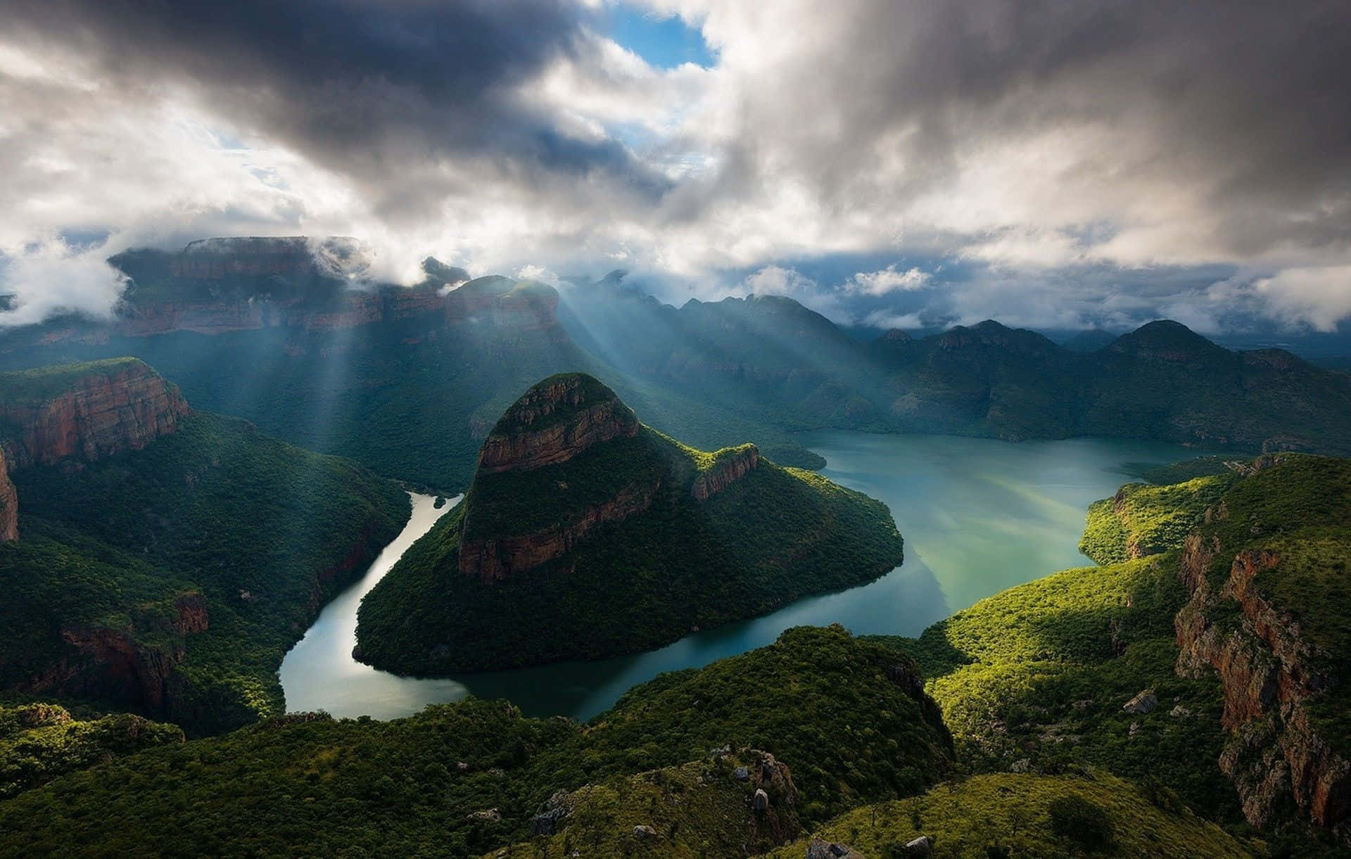 African Landscapes 桌布 壁紙 — 陽光穿透暴風雲層，照亮蜿蜒穿過翠綠山脈和岩石峭壁的河流。
