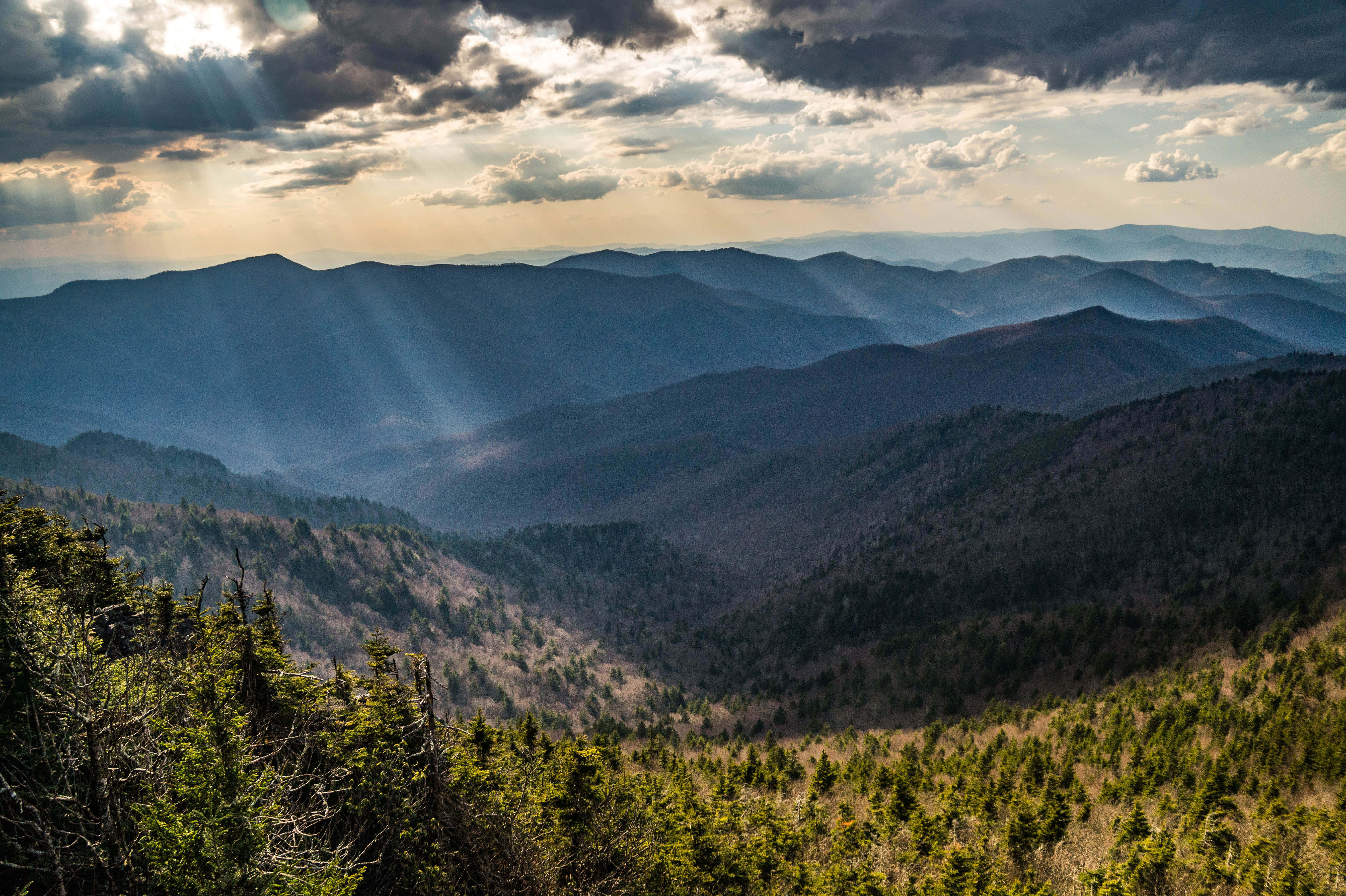 Blue Ridge Mountains 桌布 壁紙 — 陽光穿透烏雲，在層層疊疊、覆蓋著茂密森林的山脈上投射出戲劇性的光線。