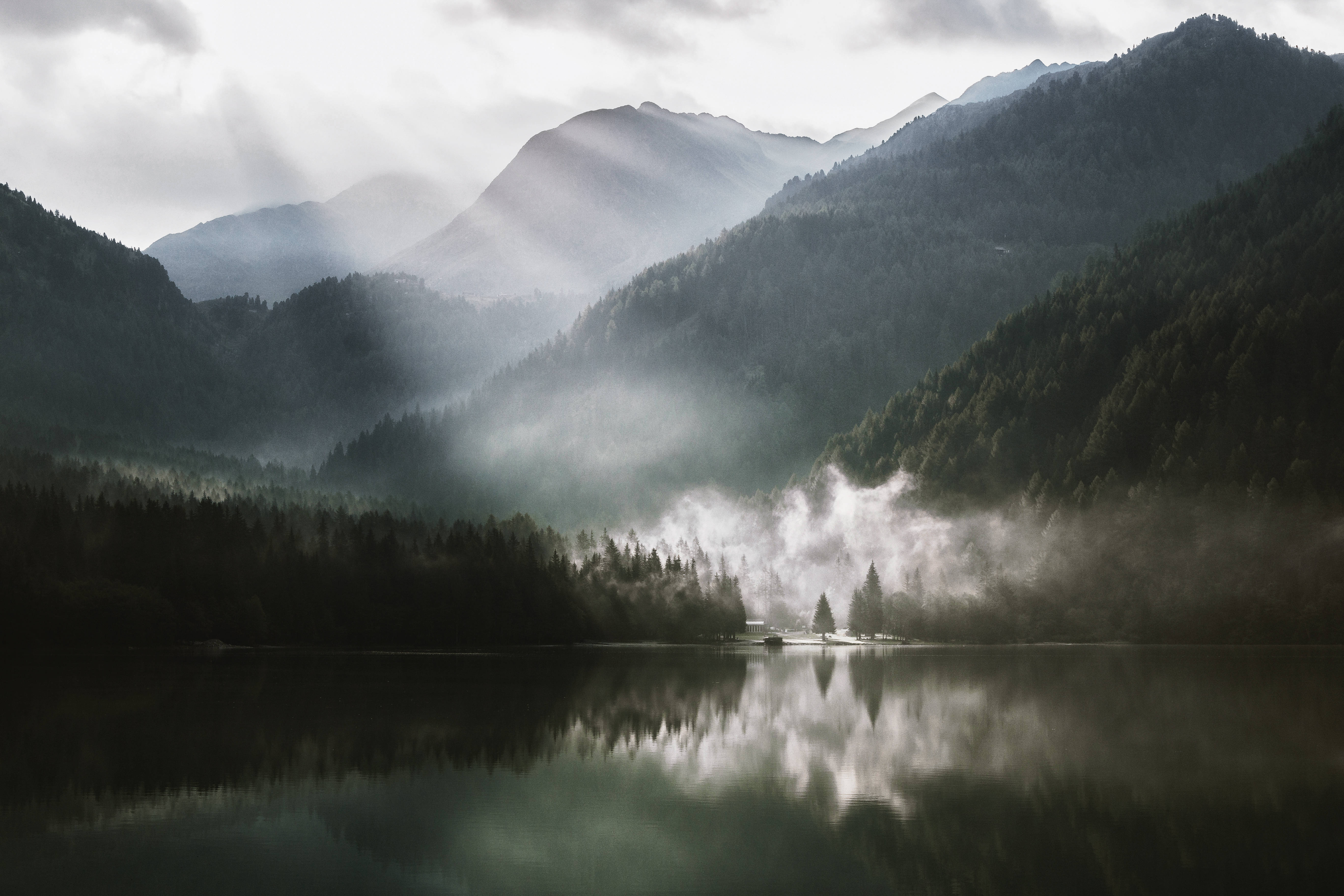 Lake 桌布 壁紙 — 陽光穿透霧氣繚繞的山巒，倒映在寧靜的湖面上，四周環繞著茂密的森林。