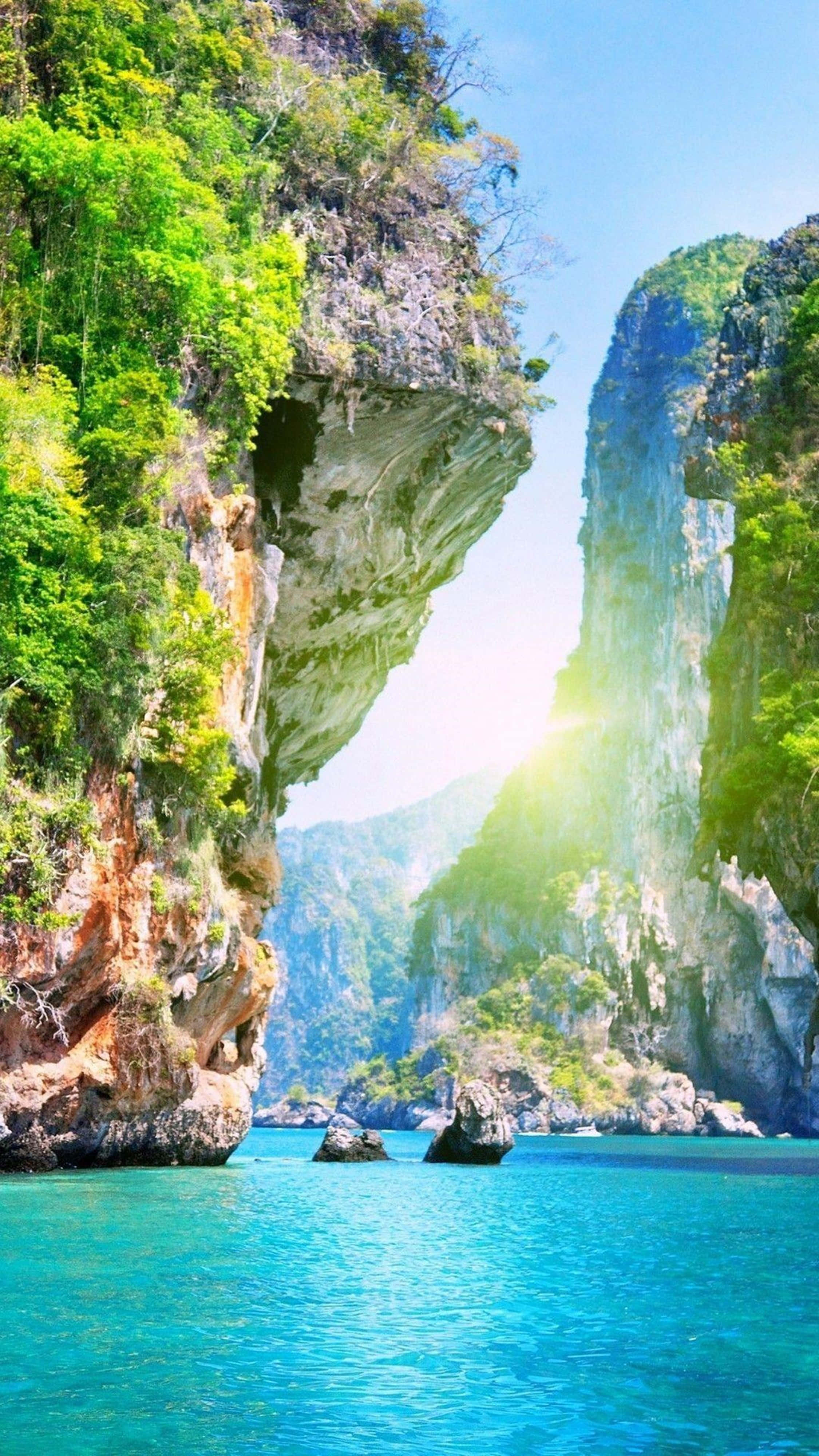 Nature Scenes 桌布 壁紙 — 陽光穿過天然岩石拱門，照射在被翠綠懸崖環繞的碧綠海水上。