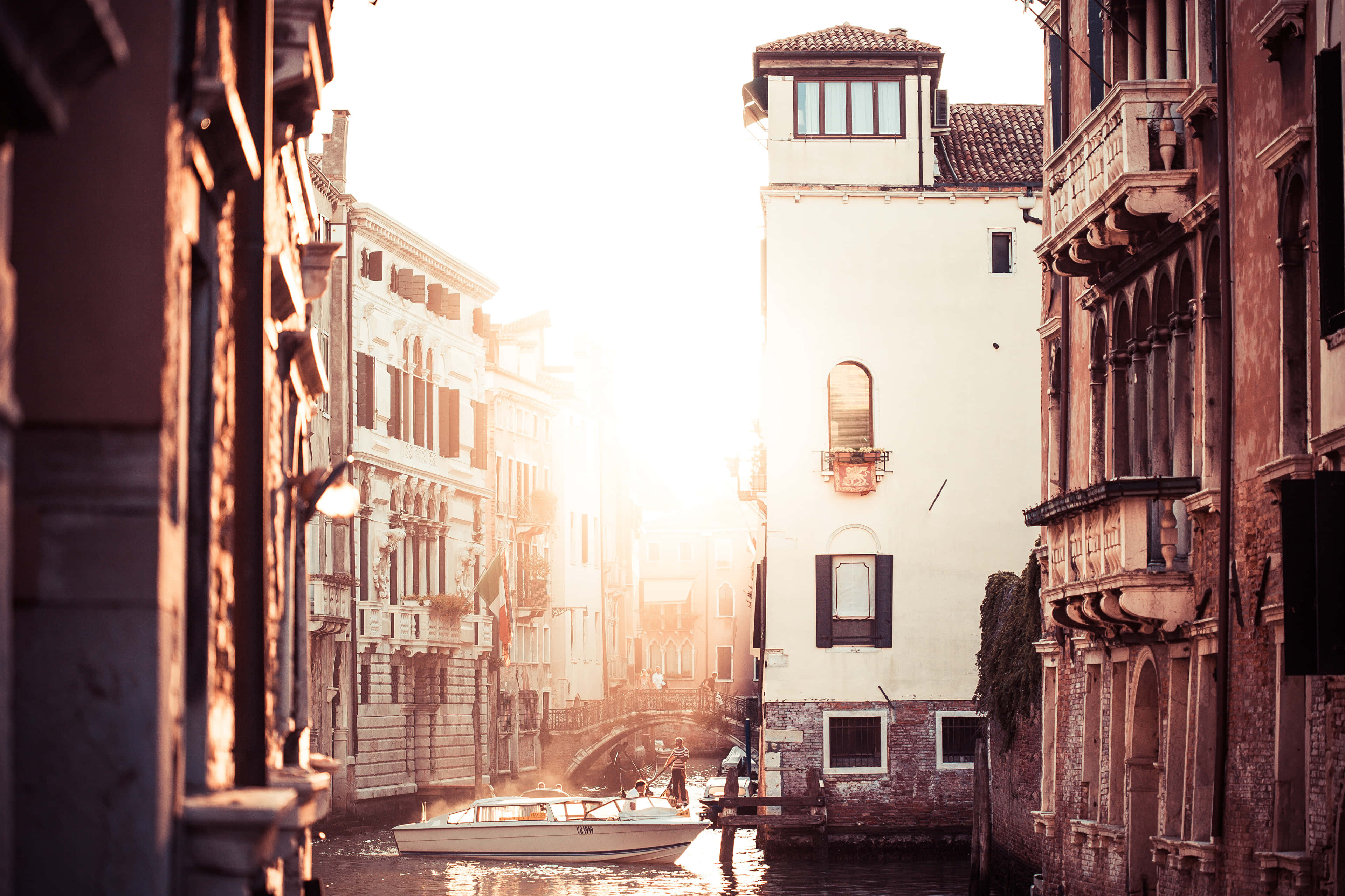 Italy Aesthetic 桌布 壁紙 — 陽光穿過威尼斯運河閃耀，一艘船飄過擁有華麗陽台的歷史建築。