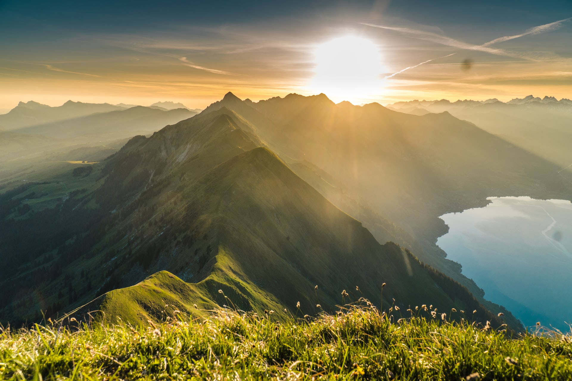 Mountain Landscape 桌布 壁紙 — 陽光穿過山峰，將金色光芒投射在寧靜的高山湖泊和鬱鬱蔥蔥的綠色山坡上。