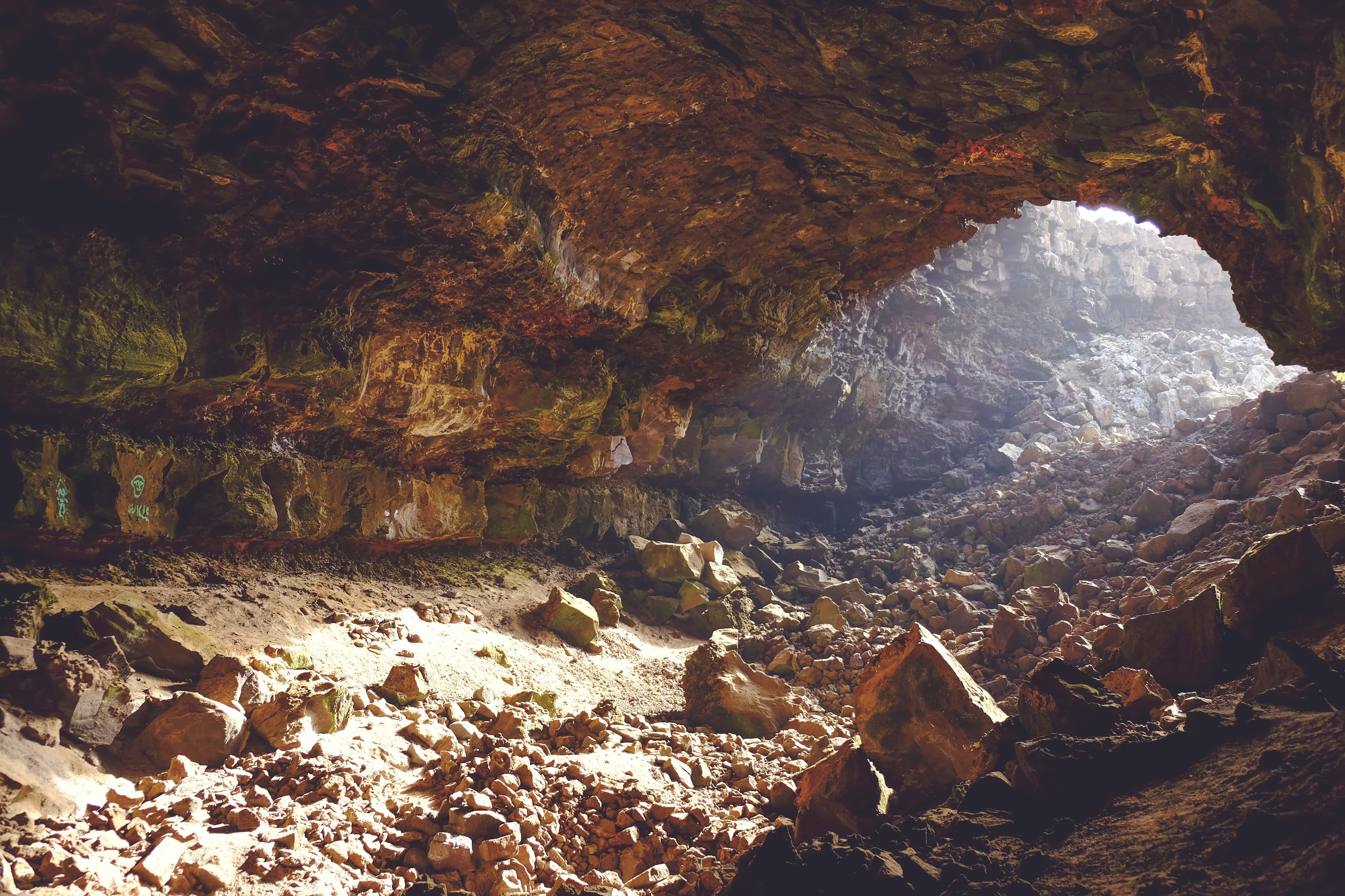 Cave 桌布 壁紙 — 陽光穿過崎嶇的洞穴開口，照亮散落的岩石和帶有大地色調的紋理牆壁。