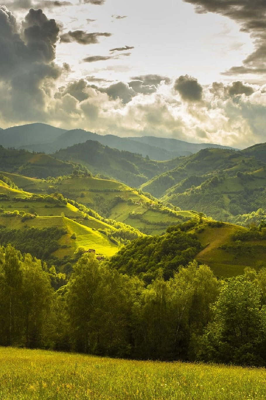 Beautiful Nature 桌布 壁紙 — 陽光穿過戲劇性的雲層，照亮了寧靜山谷中起伏的綠色山丘和森林。