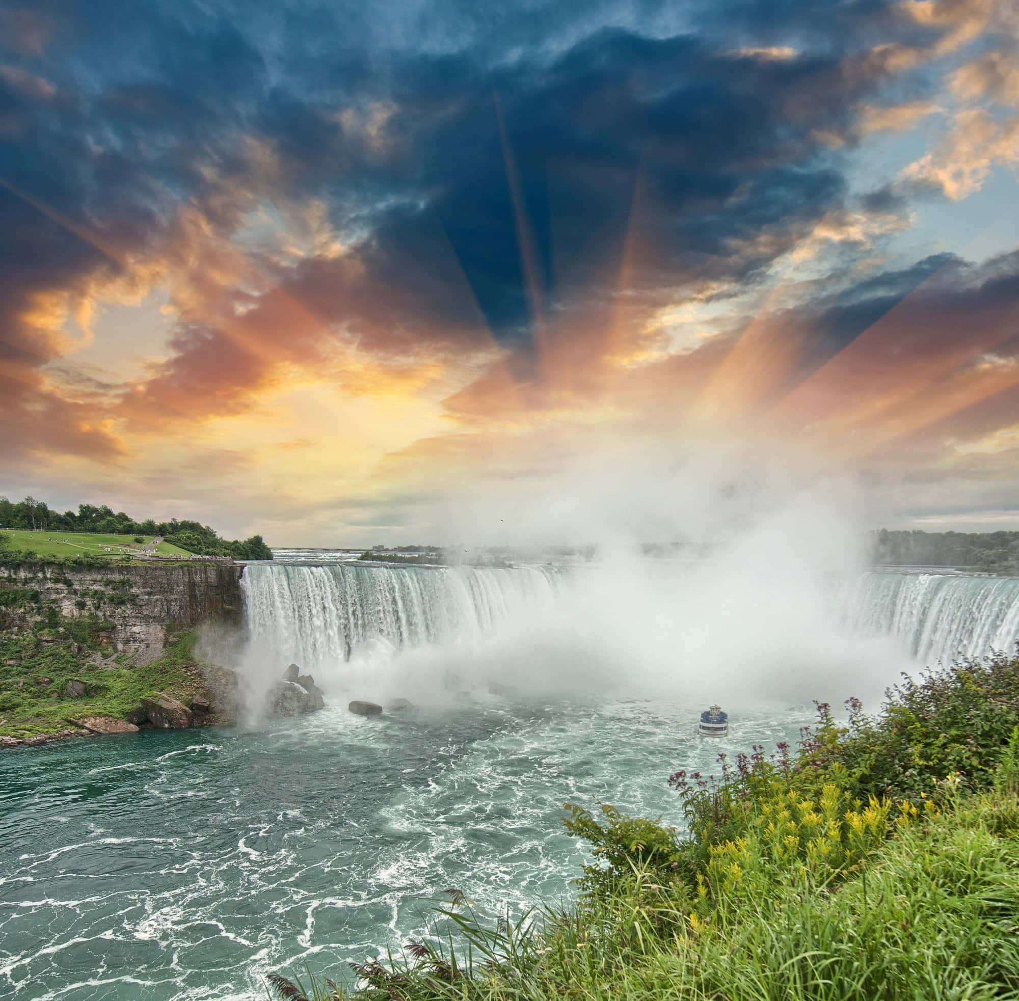 Niagara Falls 桌布 壁紙 — 陽光穿過戲劇性的雲層，照耀在咆哮的尼亞加拉大瀑布霧氣和碧綠的水面上。