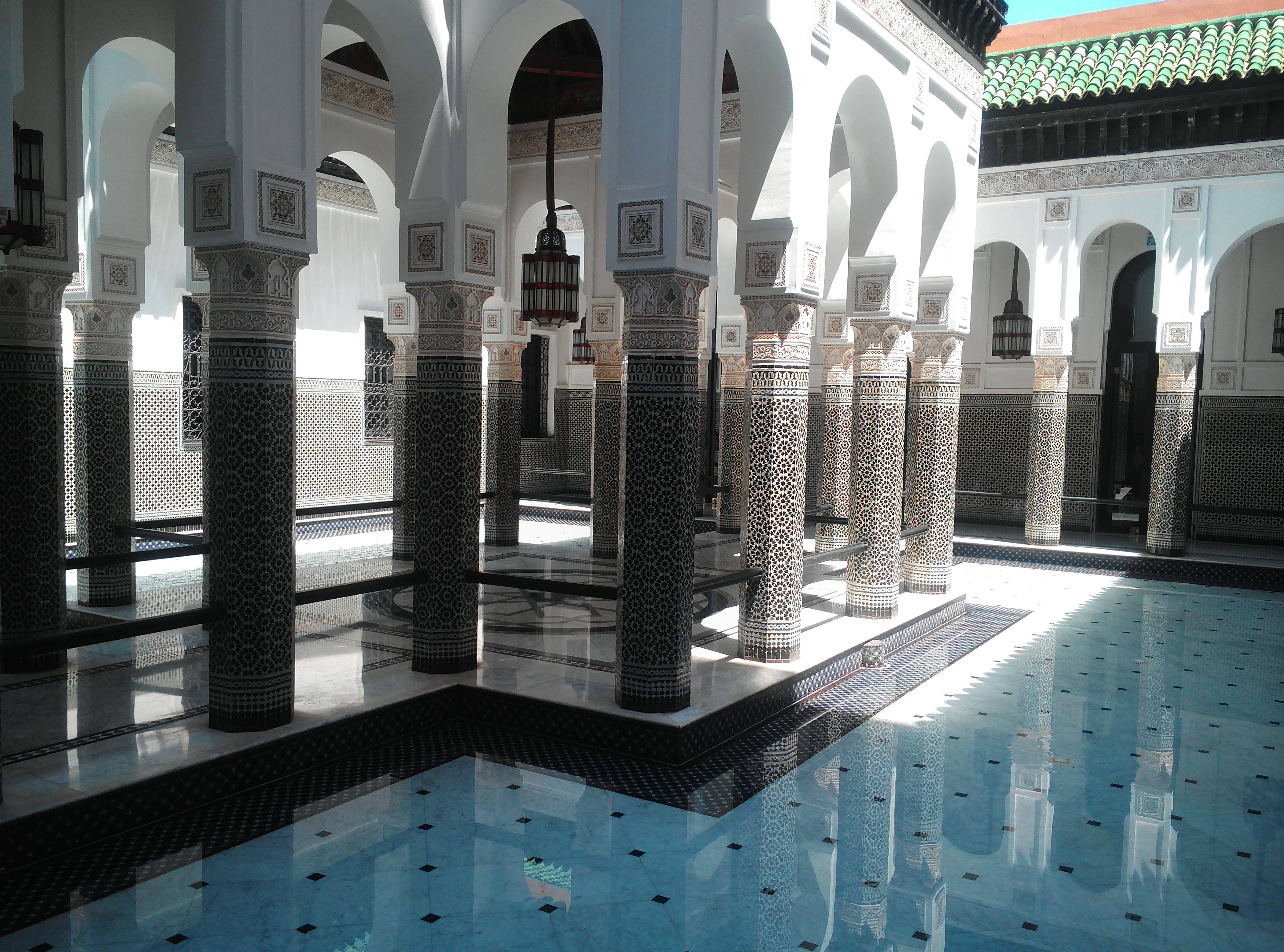 Morocco 桌布 壁紙 — 陽光穿過拱形柱廊，在鋪有複雜幾何圖案的瓷磚庭院泳池上投下倒影。