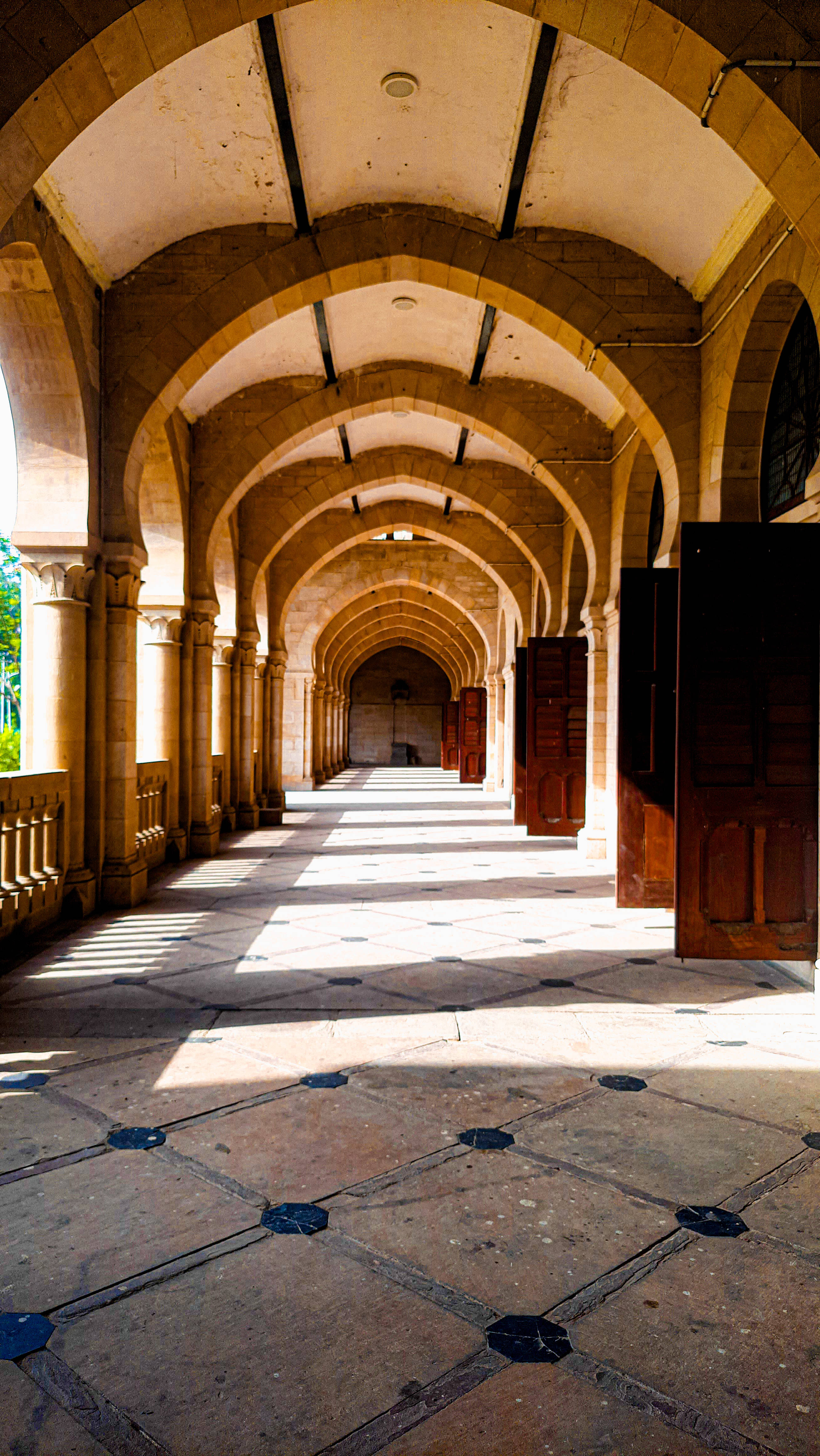 University 桌布 壁紙 — 陽光穿過拱形石柱，在宏偉的歷史走廊的圖案瓷磚地板上投下長長的陰影。
