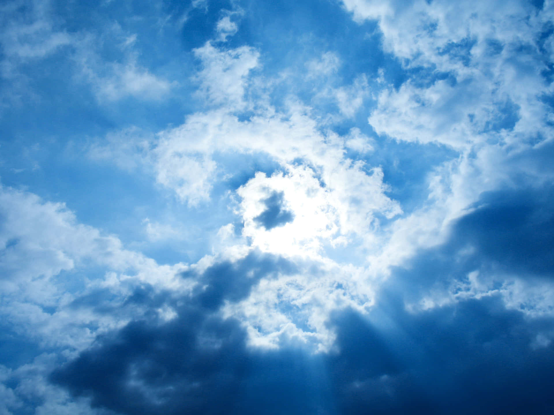 雲朵 桌布 壁紙 — 陽光穿過旋轉的藍白雲層，形成動態的天空場景。