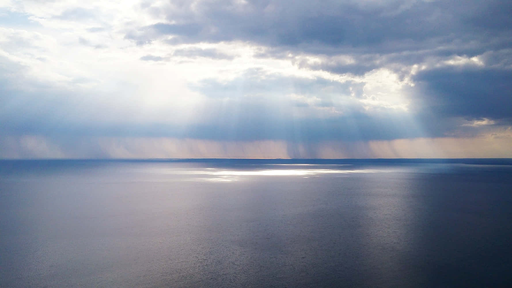 Calm 桌布 壁紙 — 陽光穿過暴風雲，在廣闊平靜的海洋地平線上投射出戲劇性的光線。