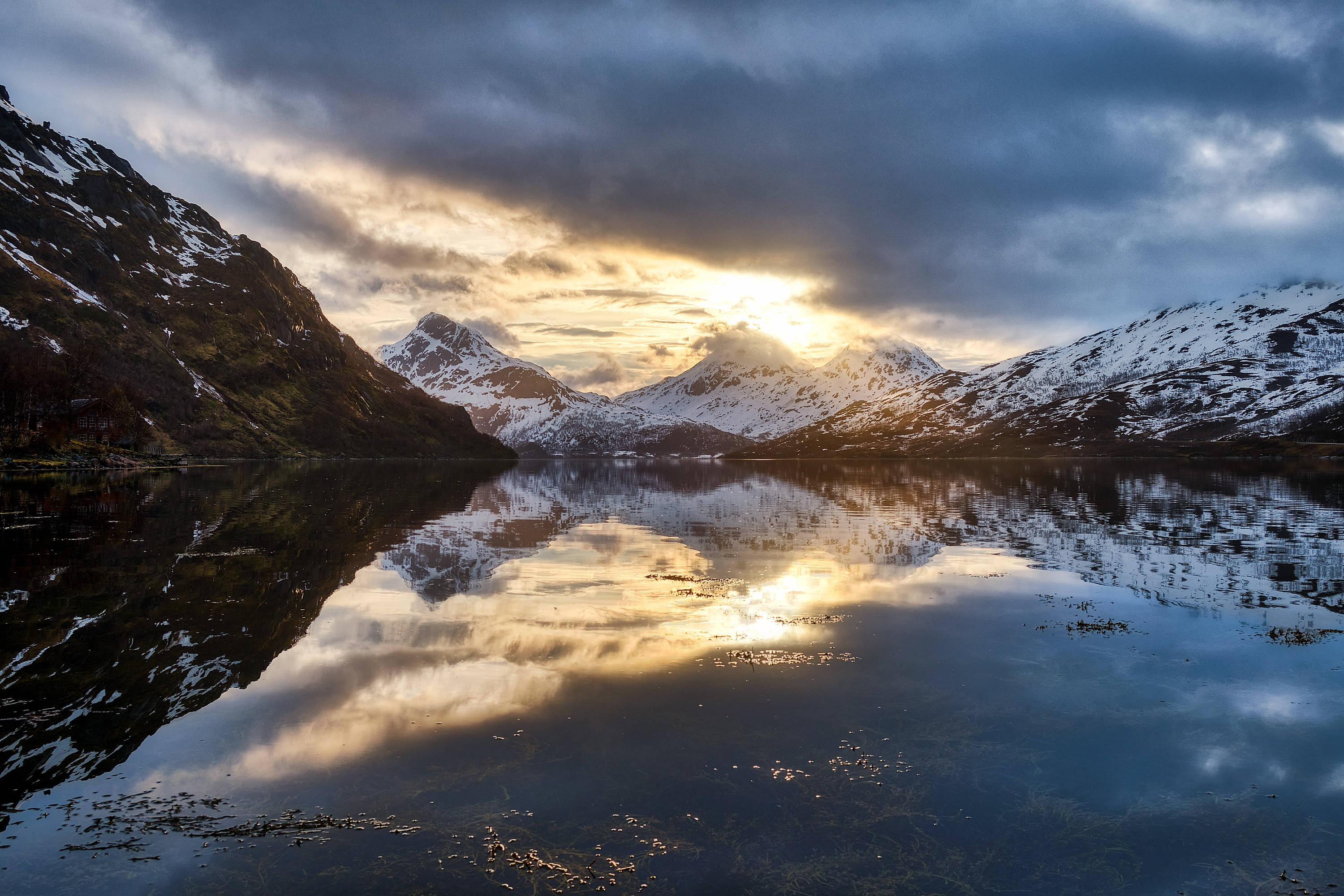 Norway 桌布 壁紙 — 陽光穿過暴風雲，將金色光芒投射在積雪的山峰上，完美地倒映在平靜的高山湖泊中。