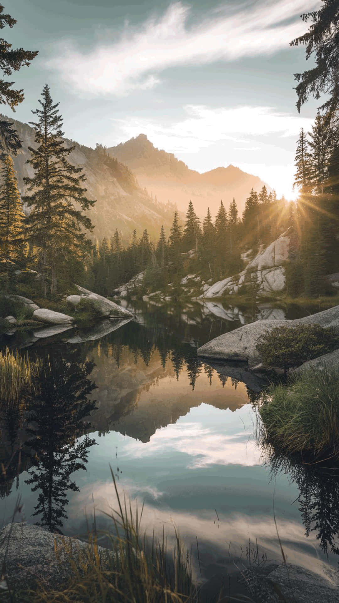 Serene mountain lake at sunrise  nature wallpaper 壁紙 — 陽光穿過松樹，照耀在平靜的山湖上，倒映出崎嶇的山峰和天空。