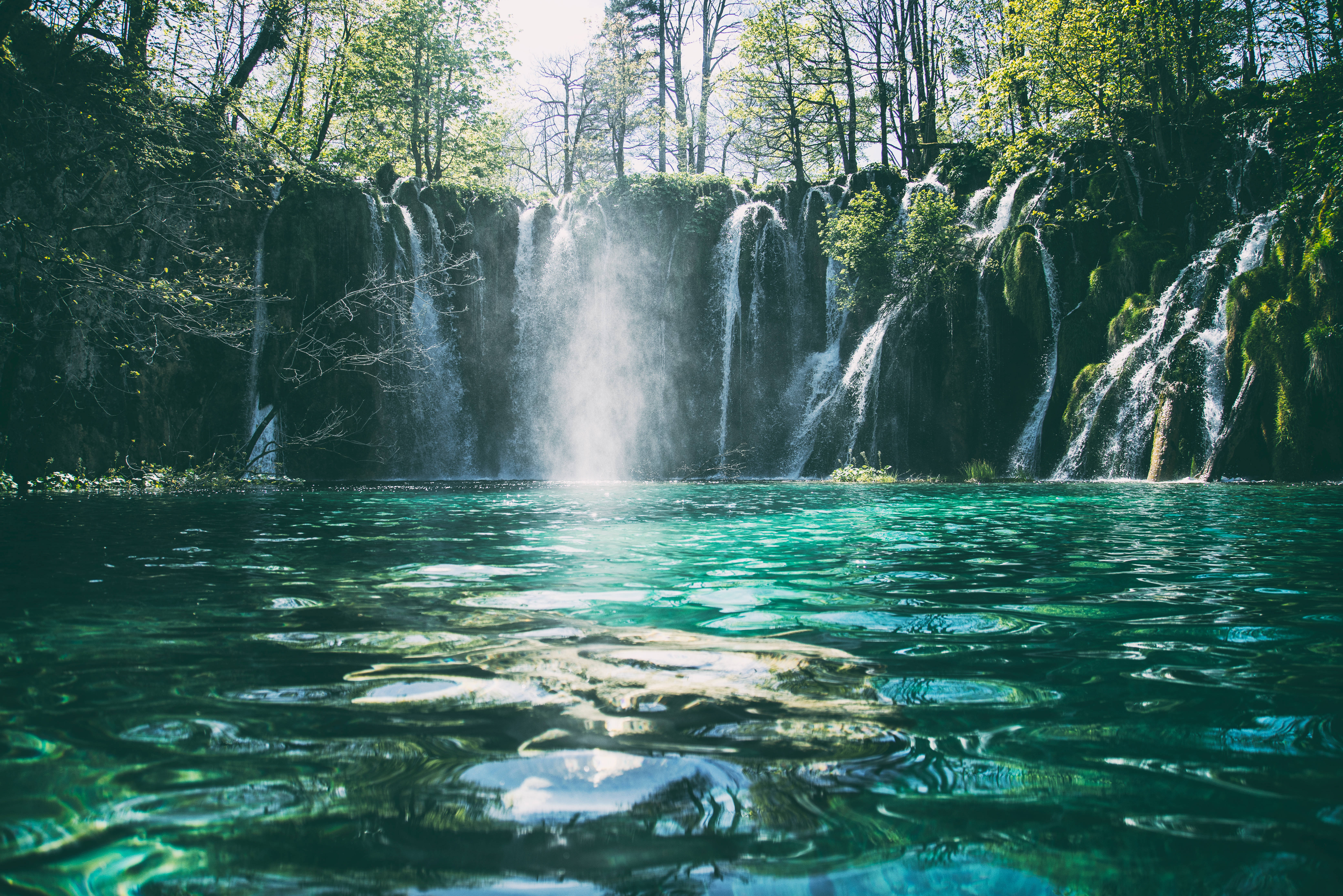 Croatia 桌布 壁紙 — 陽光穿過樹林，照亮了層疊的瀑布，流入清澈見底的碧綠水池。