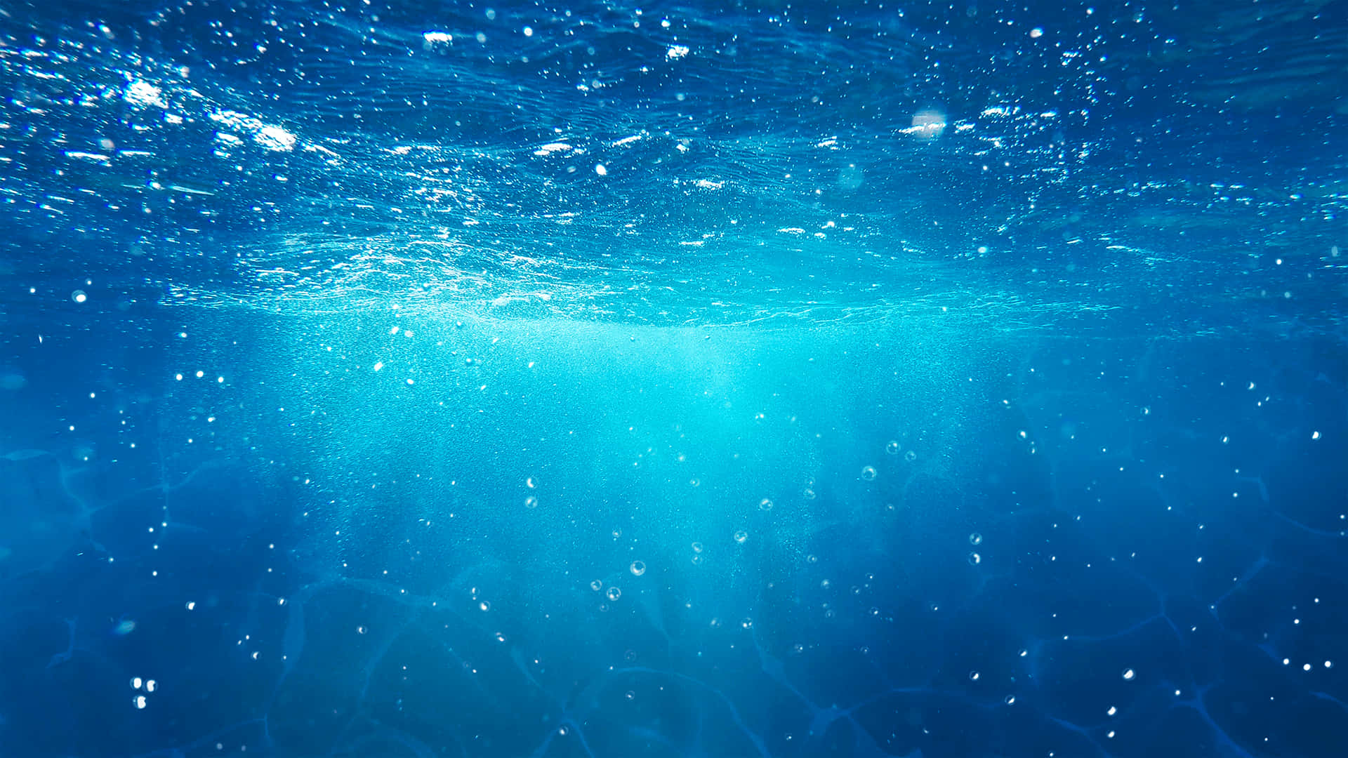 水 桌布 壁紙 — 陽光穿過清澈的藍色海水，營造出寧靜的水下場景，有浮動的氣泡和漣漪的水面。