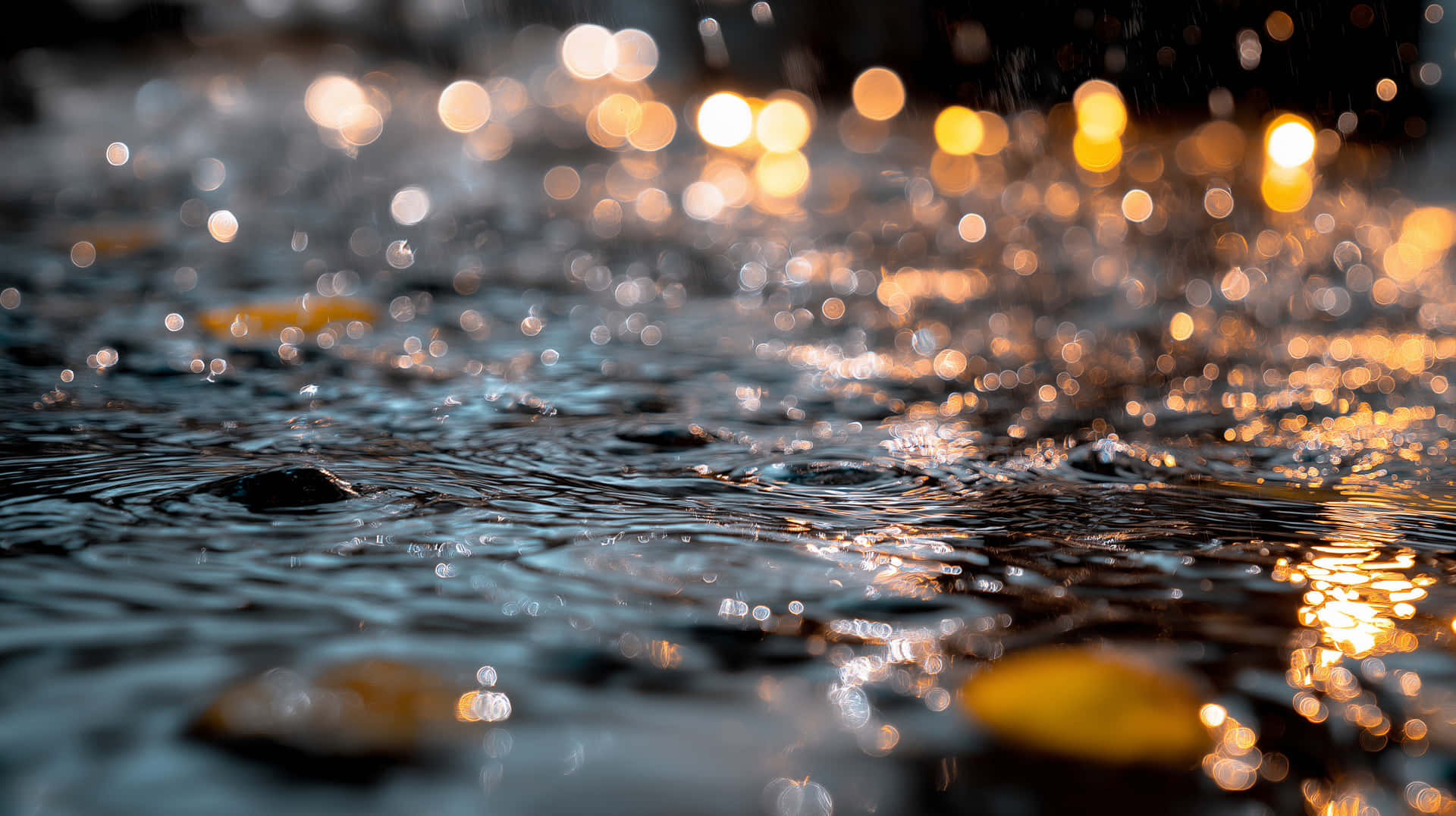 Rain Falling on Ground Creating Ripples and Golden Bokeh 壁紙 — 陽光穿過漣漪水面上的雨滴閃爍，在黑暗漣漪上形成金色散景。