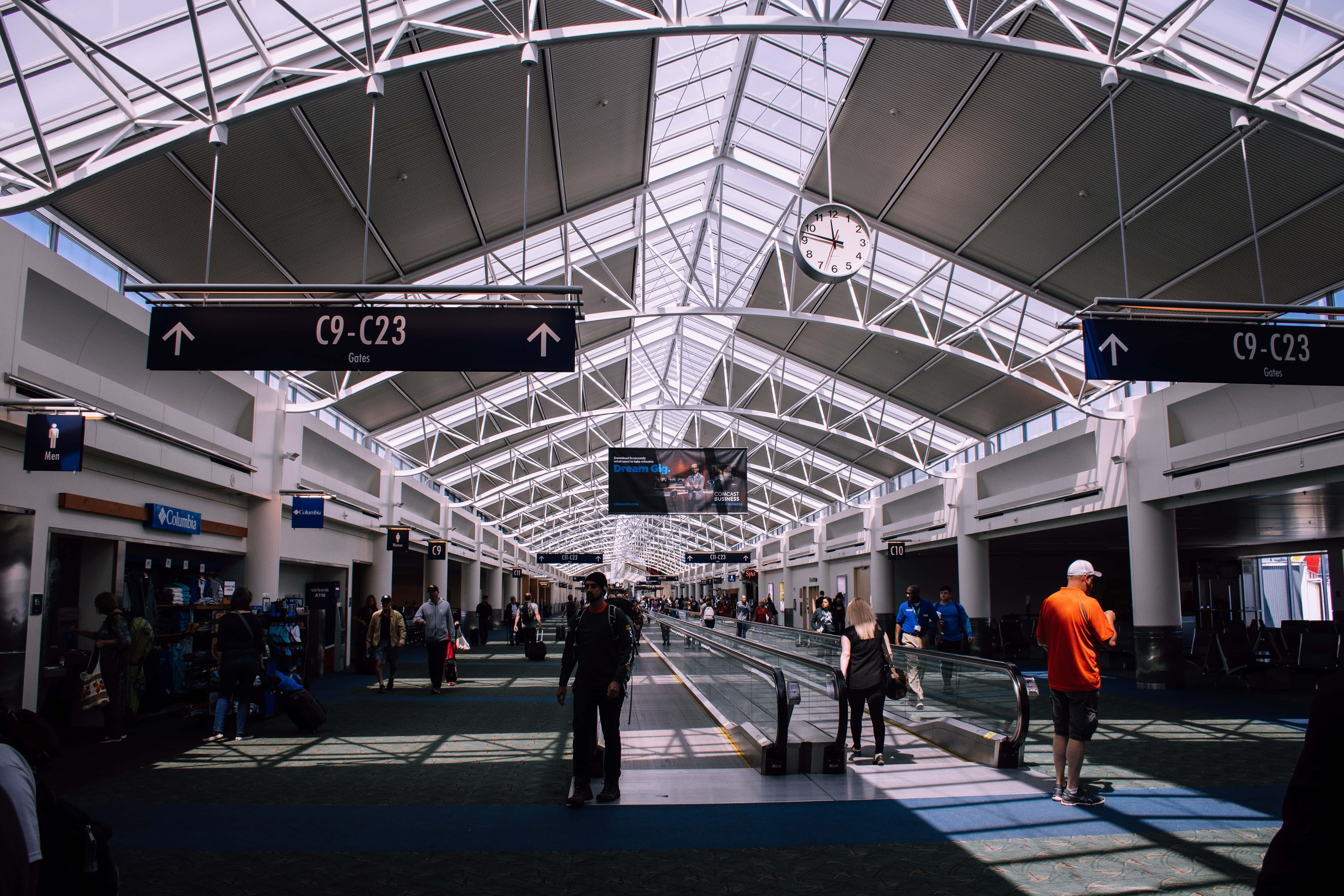 Airport 桌布 壁紙 — 陽光穿過玻璃天花板，照亮現代機場航廈自動人行道上的旅客。