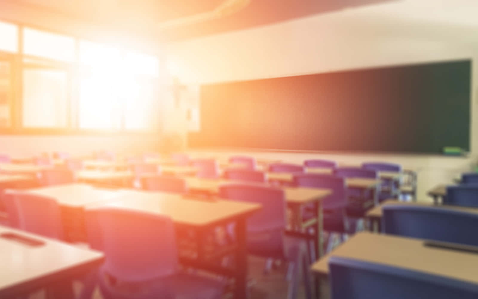 Real Classroom 桌布 壁紙 — 陽光穿過窗戶，照亮了一個模糊的教室，裡面有排列整齊的書桌和一塊黑板。