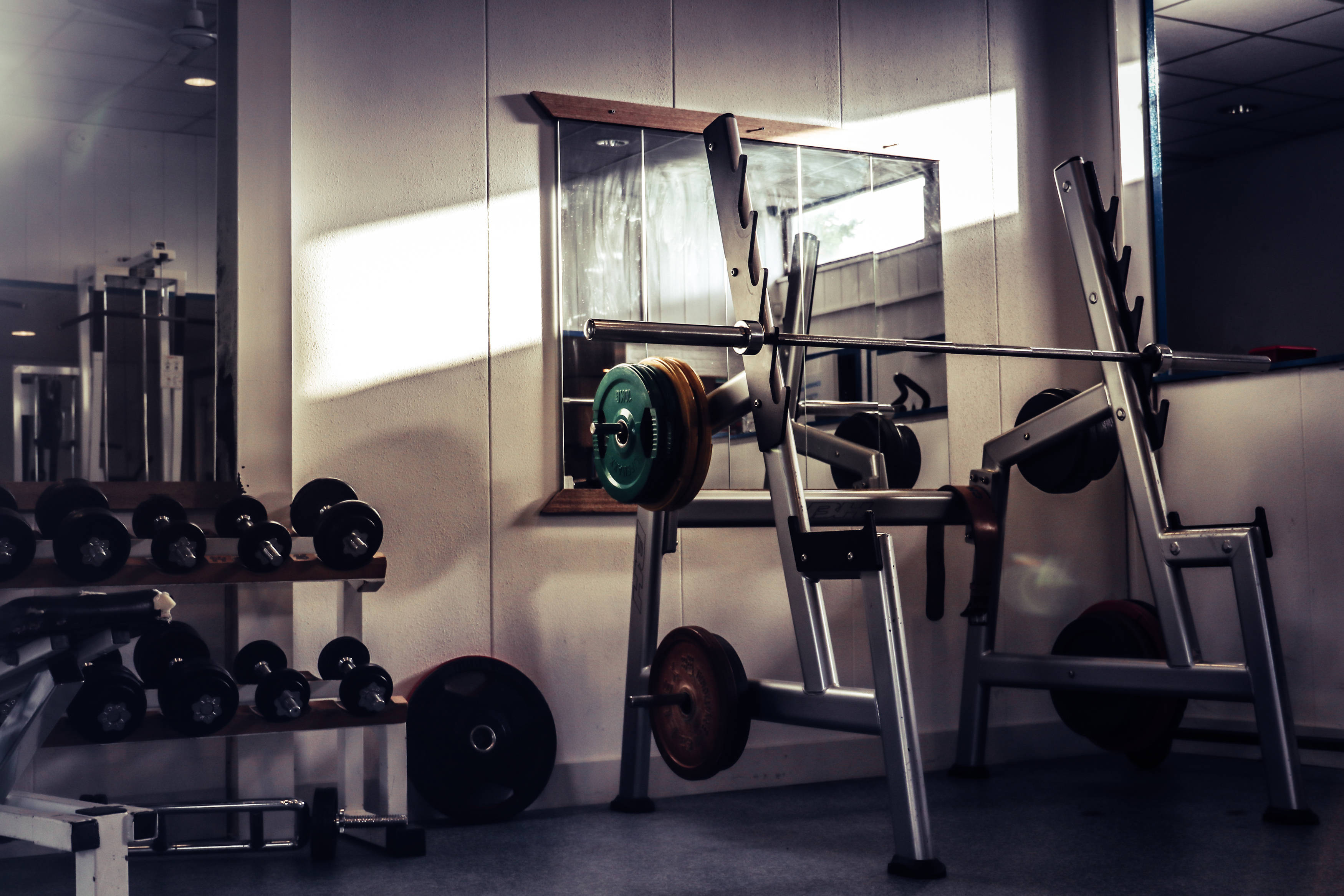 Fitness 桌布 壁紙 — 陽光穿過窗戶照射著健身器材，包括啞鈴、槓鈴和重量架，在一個安靜的健身空間中。