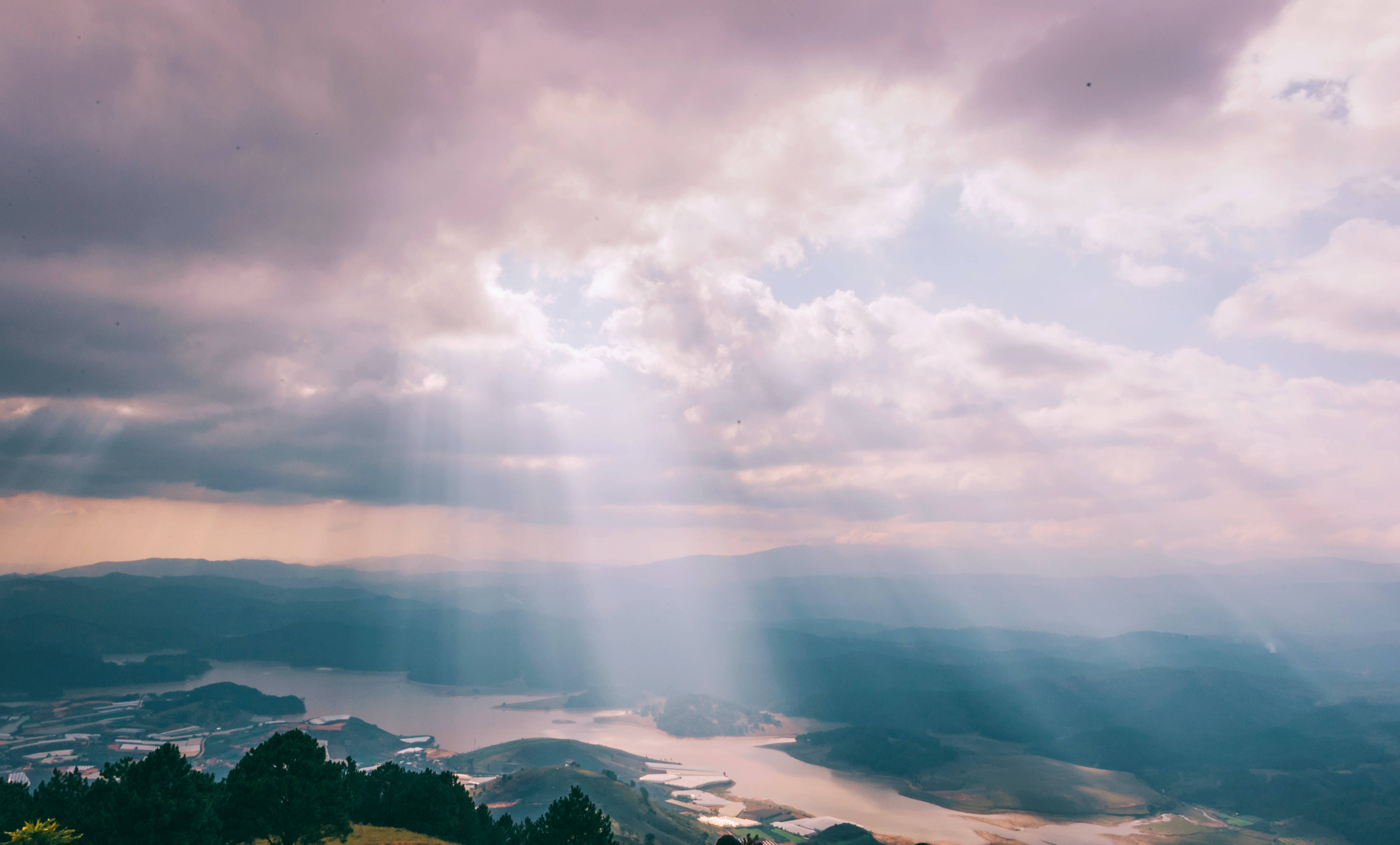 Sun Rays 桌布 壁紙 — 陽光穿過紫色雲層，將神聖的光芒投射在薄霧籠罩的山谷上，山谷中有蜿蜒的河流和遠山。